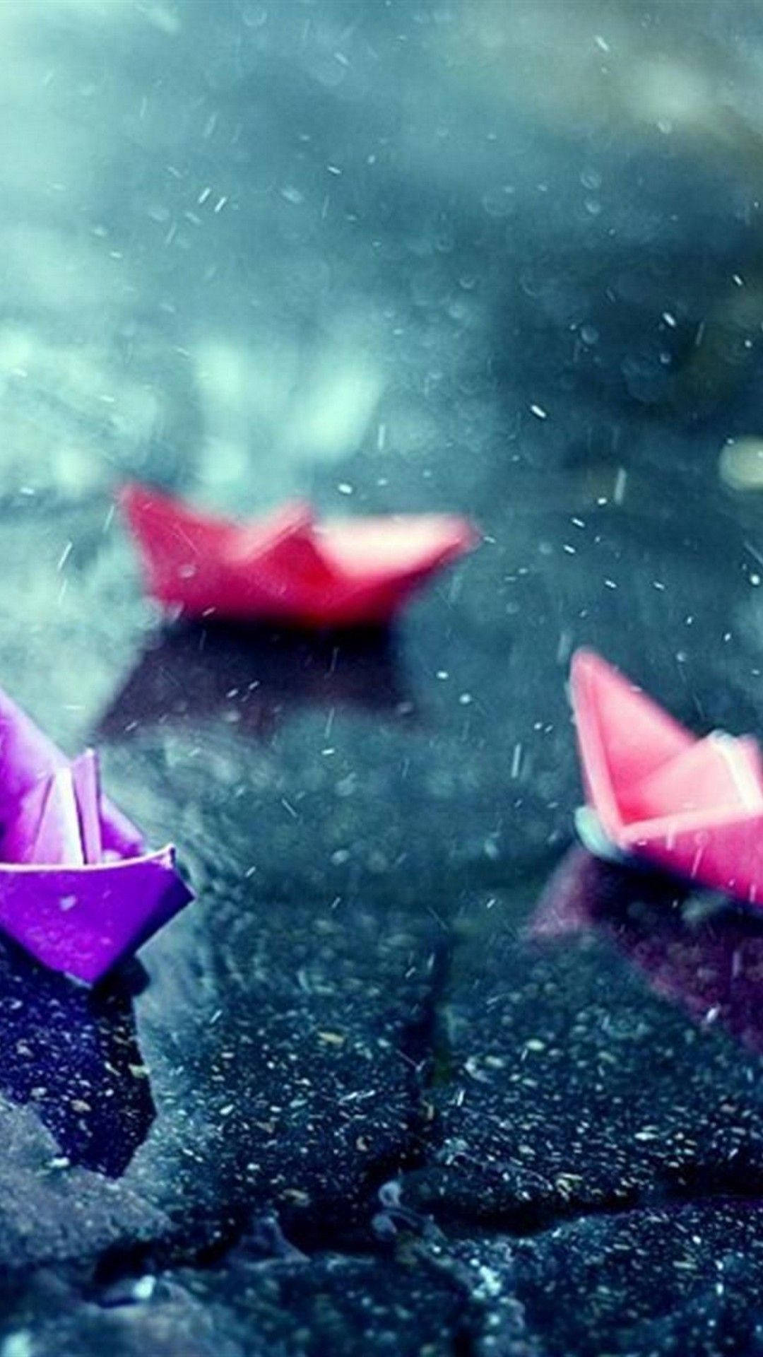 雨中 iPhone 的一瞥 壁紙 — 鮮豔的粉紅色和紫色紙船在雨水浸濕的黑暗表面上輕輕漂浮，落下的水滴營造出憂鬱的氛圍。