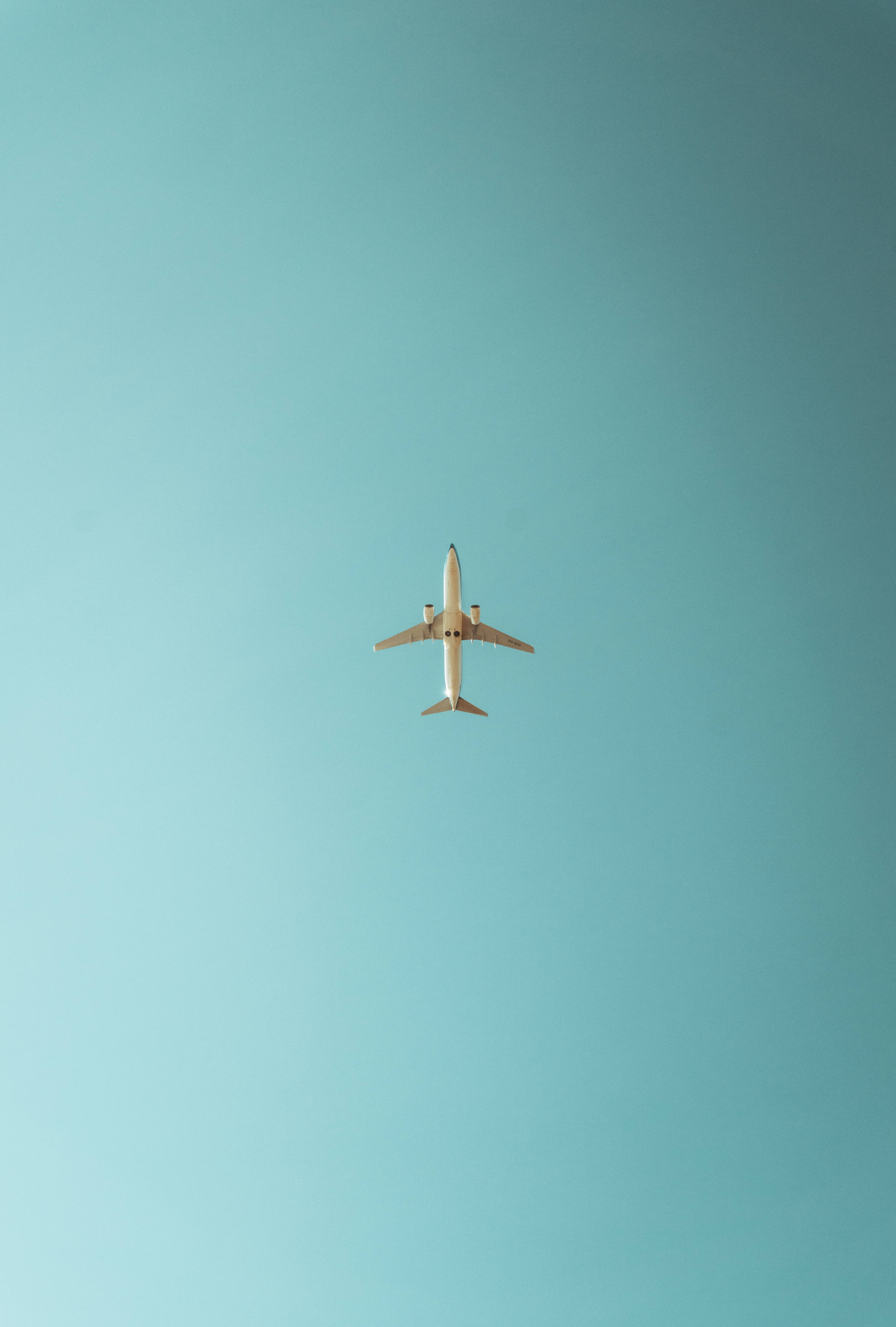 極簡飛機 iPhone 壁紙 — 一架白色飛機在廣闊清澈的藍綠色天空中獨自翱翔，構成極簡風格。
