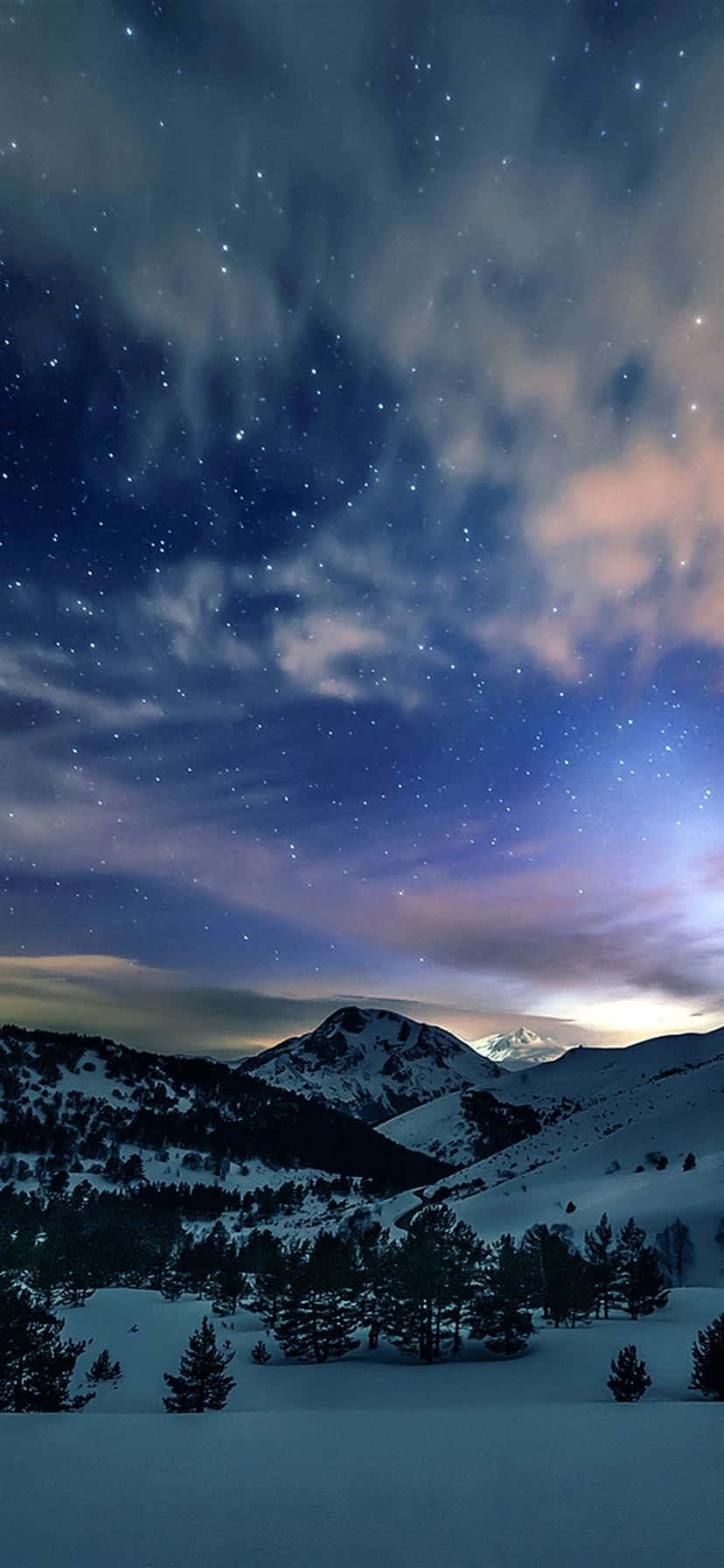 「iPhone 捕捉的迷人冬季仙境」 壁紙 — 白雪覆蓋的山峰，在繁星點點的夜空下，伴隨著柔和粉紅色和藍色的雲彩。