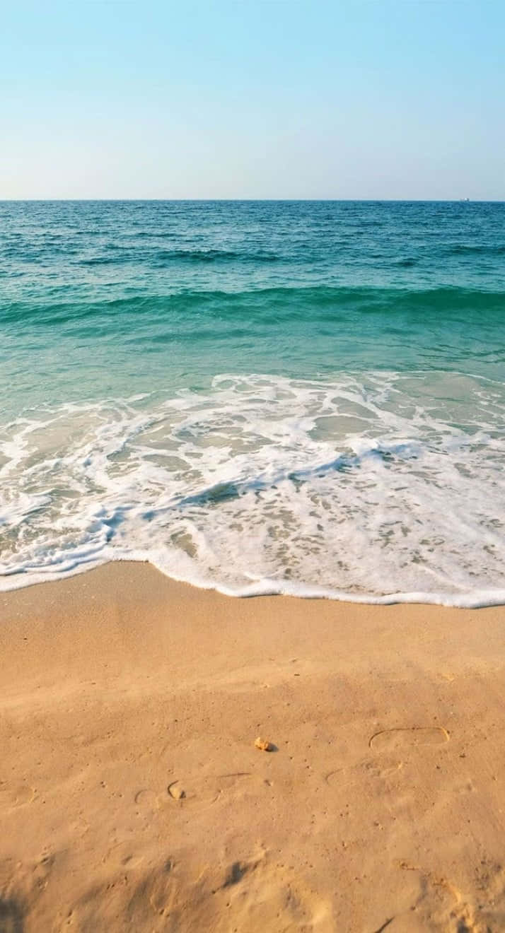 夏日海灘 iPhone 海浪 壁紙 — 平靜的碧綠海浪輕輕拍打著陽光普照的金色沙灘，天空湛藍清澈。