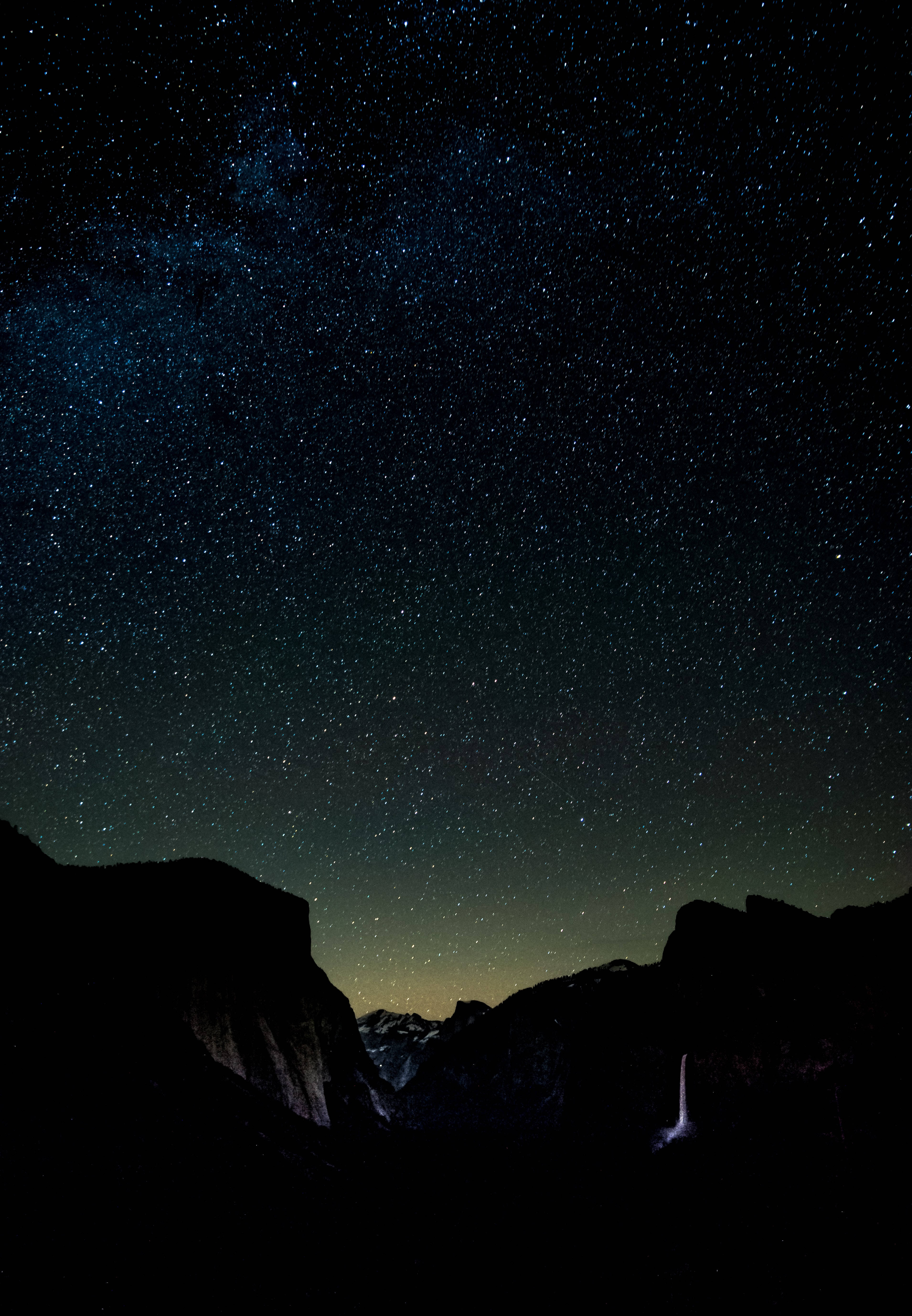 黑色iPhone拍攝的壯麗夜空景色 壁紙 — 令人屏息的夜空，佈滿無數星辰，銀河在黑暗的山谷上方拱起，映照著發光的瀑布。