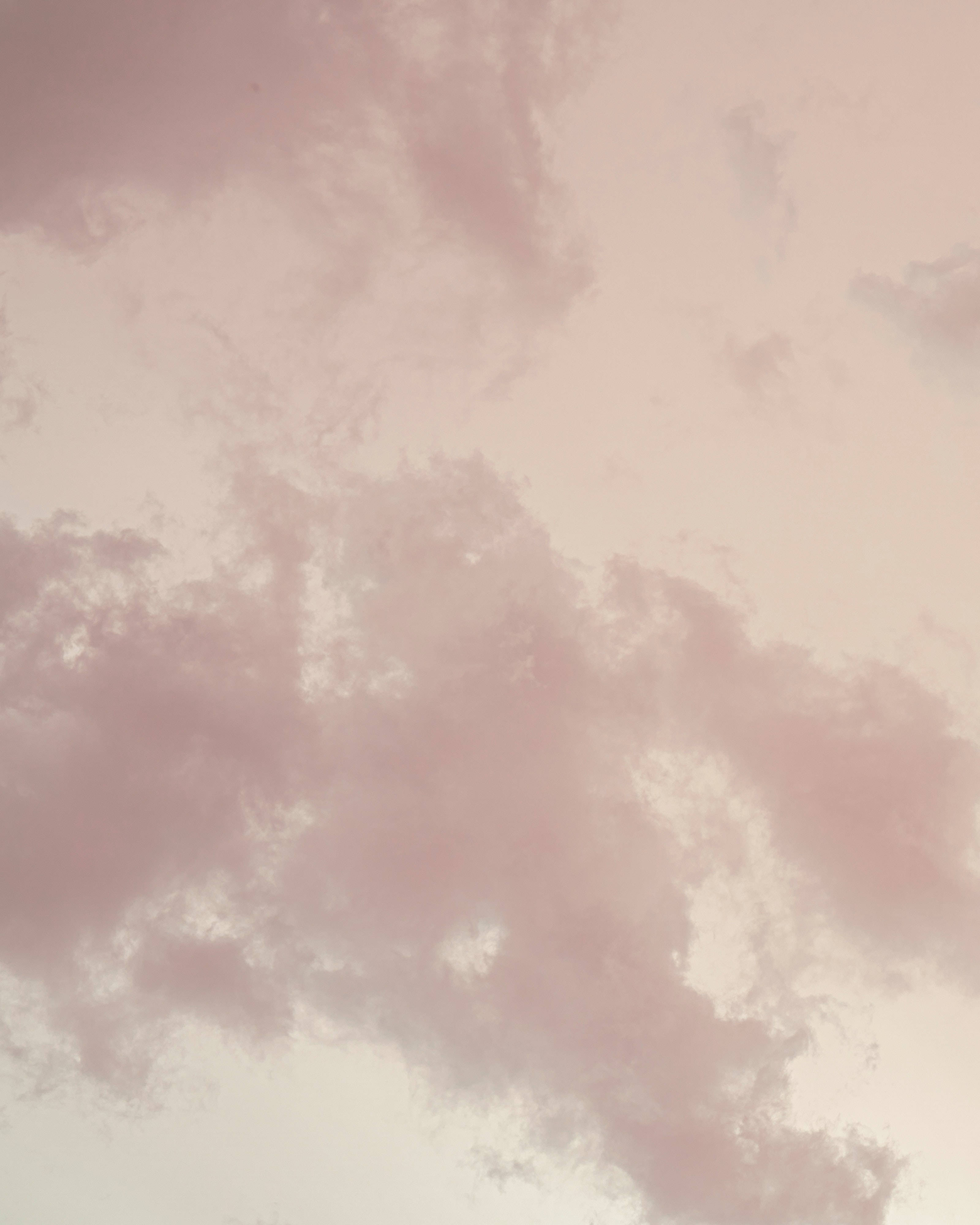 iPhone 屏幕上的寧靜雲景 壁紙 — 柔軟的粉紅雲朵在蒼白的天空中飄移，構成夢幻的粉彩日落場景。