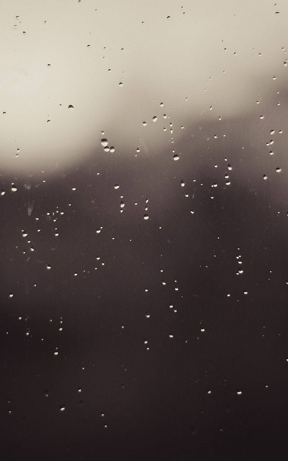 灰調iPhone雨滴窗戶壁紙 壁紙 — 雨滴依附在玻璃窗上，陰沉天空透出柔和的灰色光線。