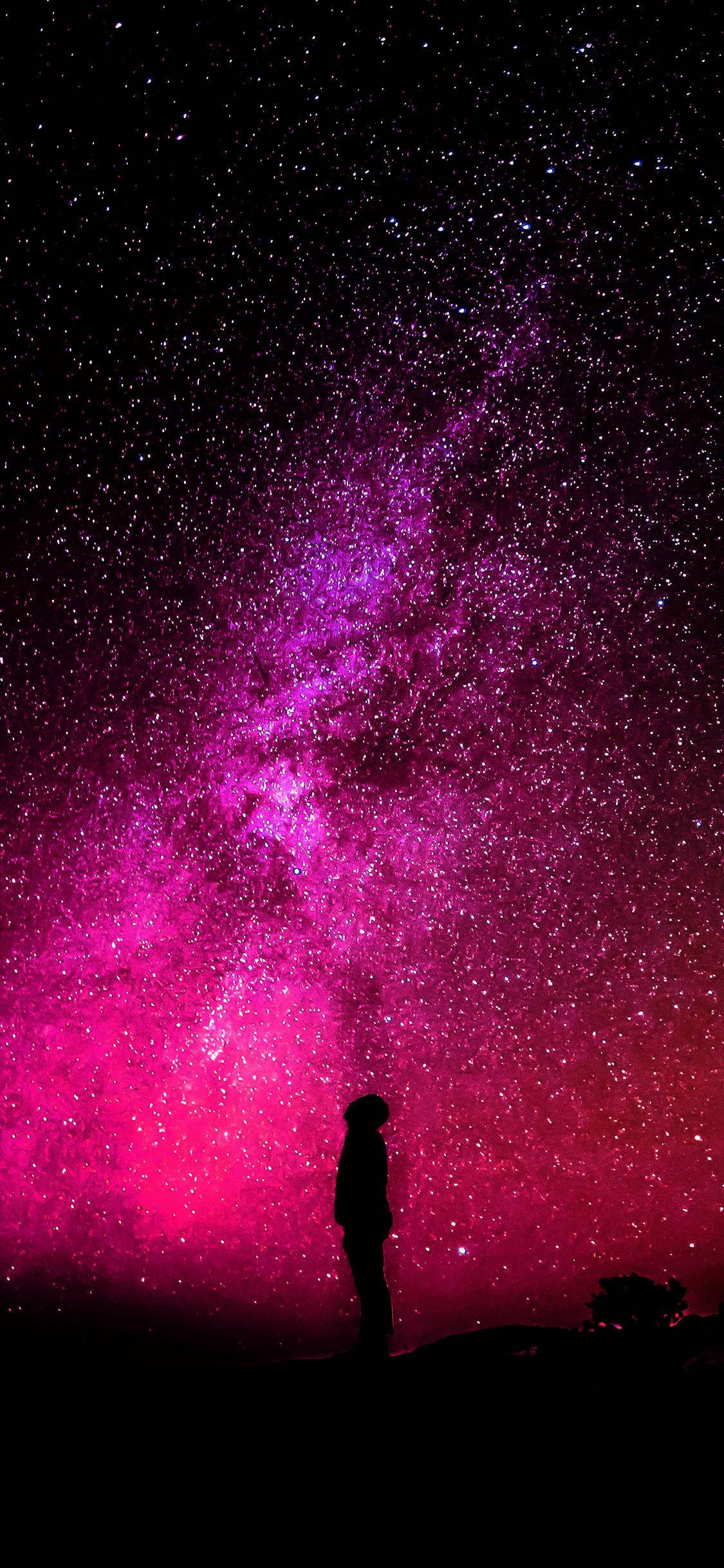 男子剪影粉紅銀河 iPhone 壁紙 — 一個孤獨的身影在令人嘆為觀止的粉紅色和紫色銀河下，敬畏地站在繁星點點的夜空下。