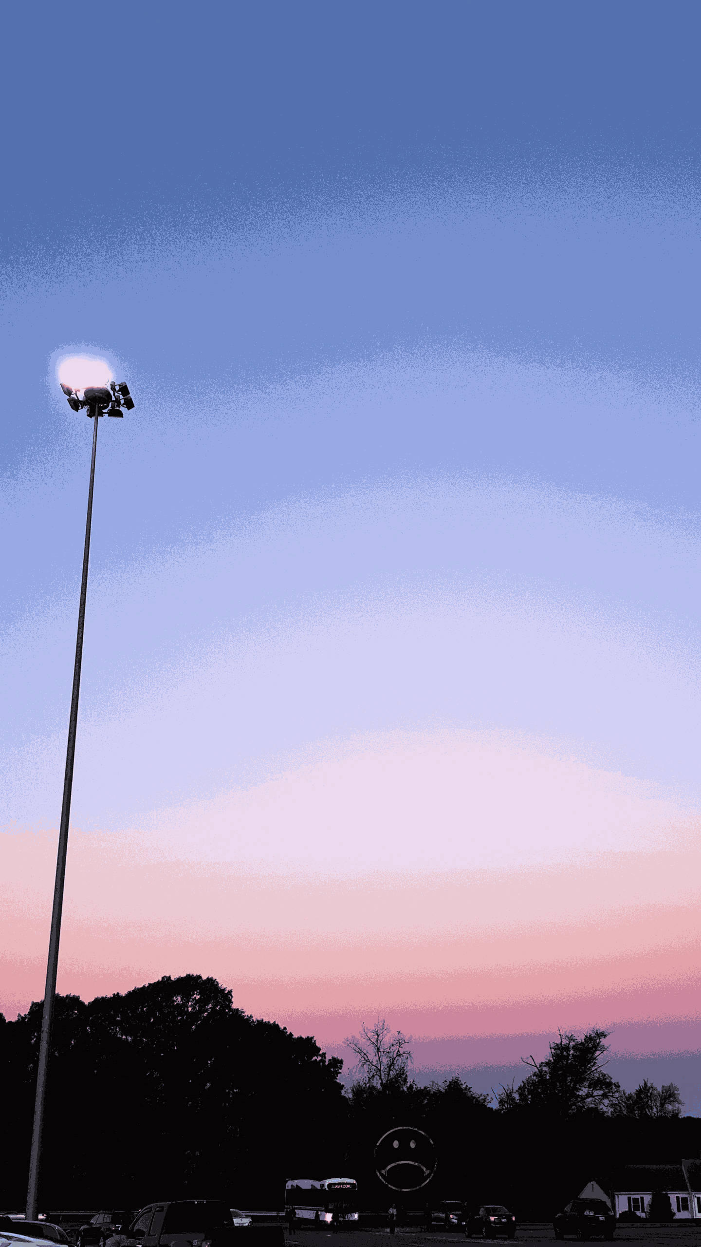 iPhone粉紅美學街道 壁紙 — 一支高大的體育場燈柱聳立在暮色天空下，天空塗上柔和的粉紅和藍色調，下方有剪影般的樹木和汽車。