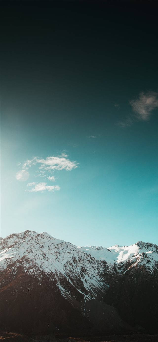 雪山 iPhone iOS 10 壁紙 — 積雪的山峰在廣闊的藍綠色天空和零星雲朵下聳立。
