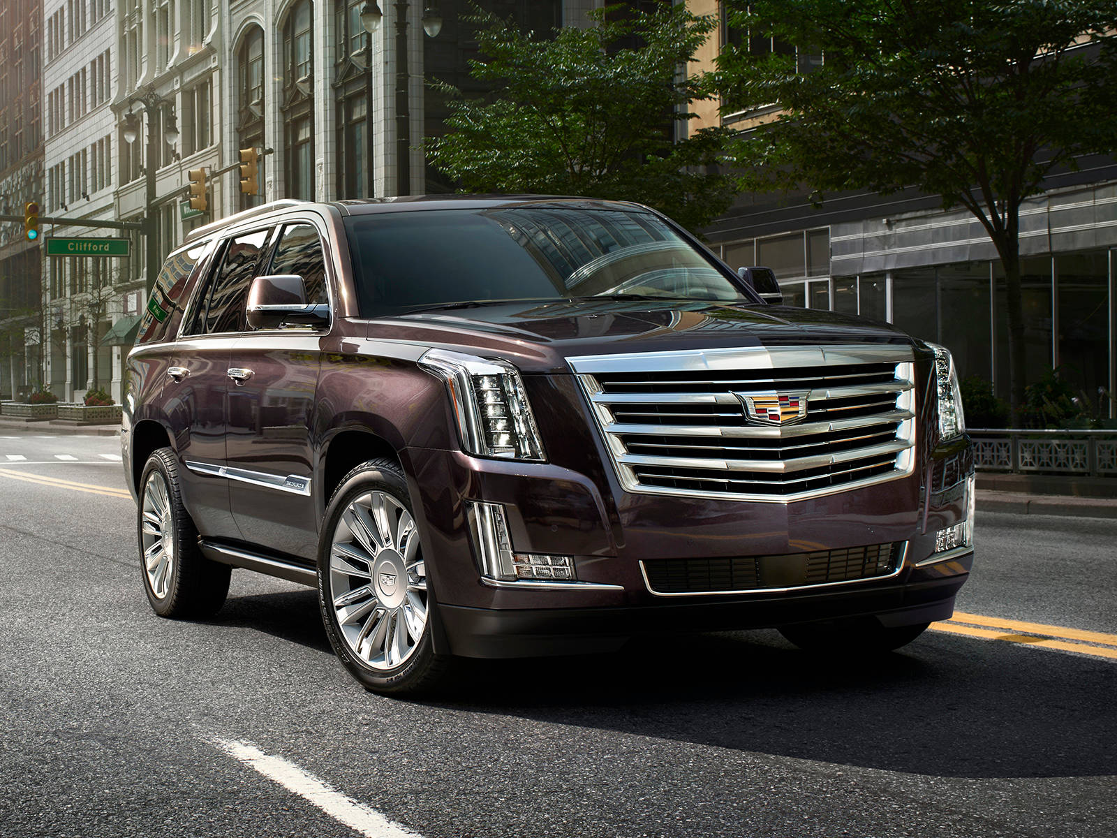 iPhone拍攝的道路上的凱迪拉克 壁紙 — 一輛光澤的栗色Cadillac Escalade SUV停泊在陽光普照的城市街道上，背景是歷史建築和綠樹。