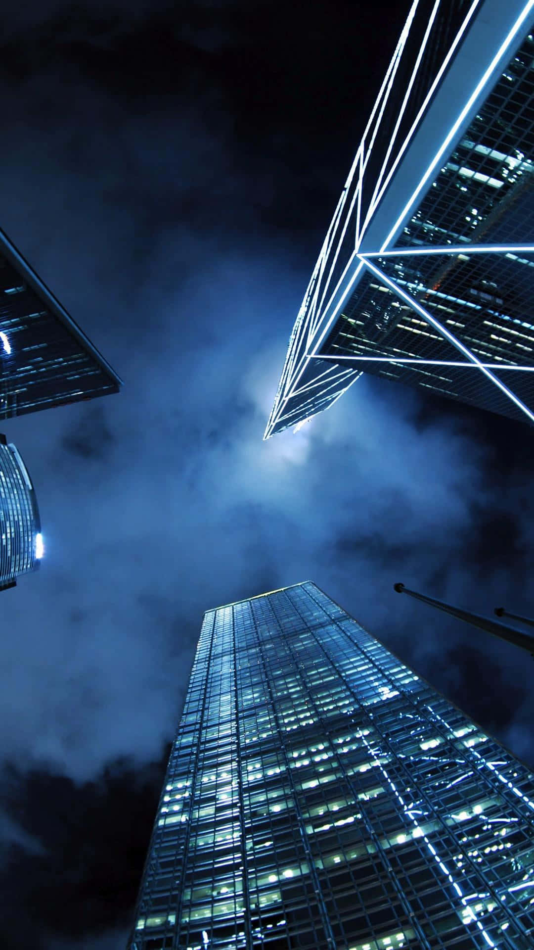 現代iPhone的優雅風采 壁紙 — 高聳入雲的摩天大樓刺穿陰沉的夜空，玻璃外牆在旋轉的雲層中閃爍著電光藍色的光芒。