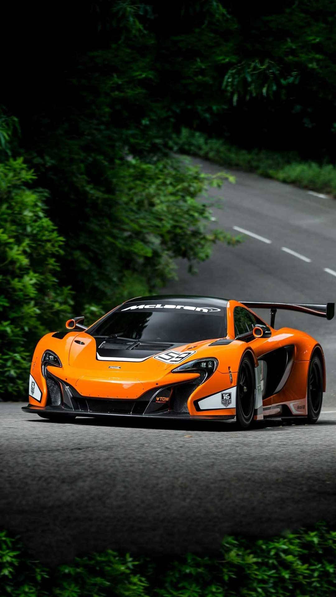 城市天際線與黑色蘭博基尼跑車 iPhone 壁紙 — 一輛充滿活力的橙色McLaren賽車在蜿蜒的森林道路上疾馳，周圍環繞著茂密的綠色樹葉。