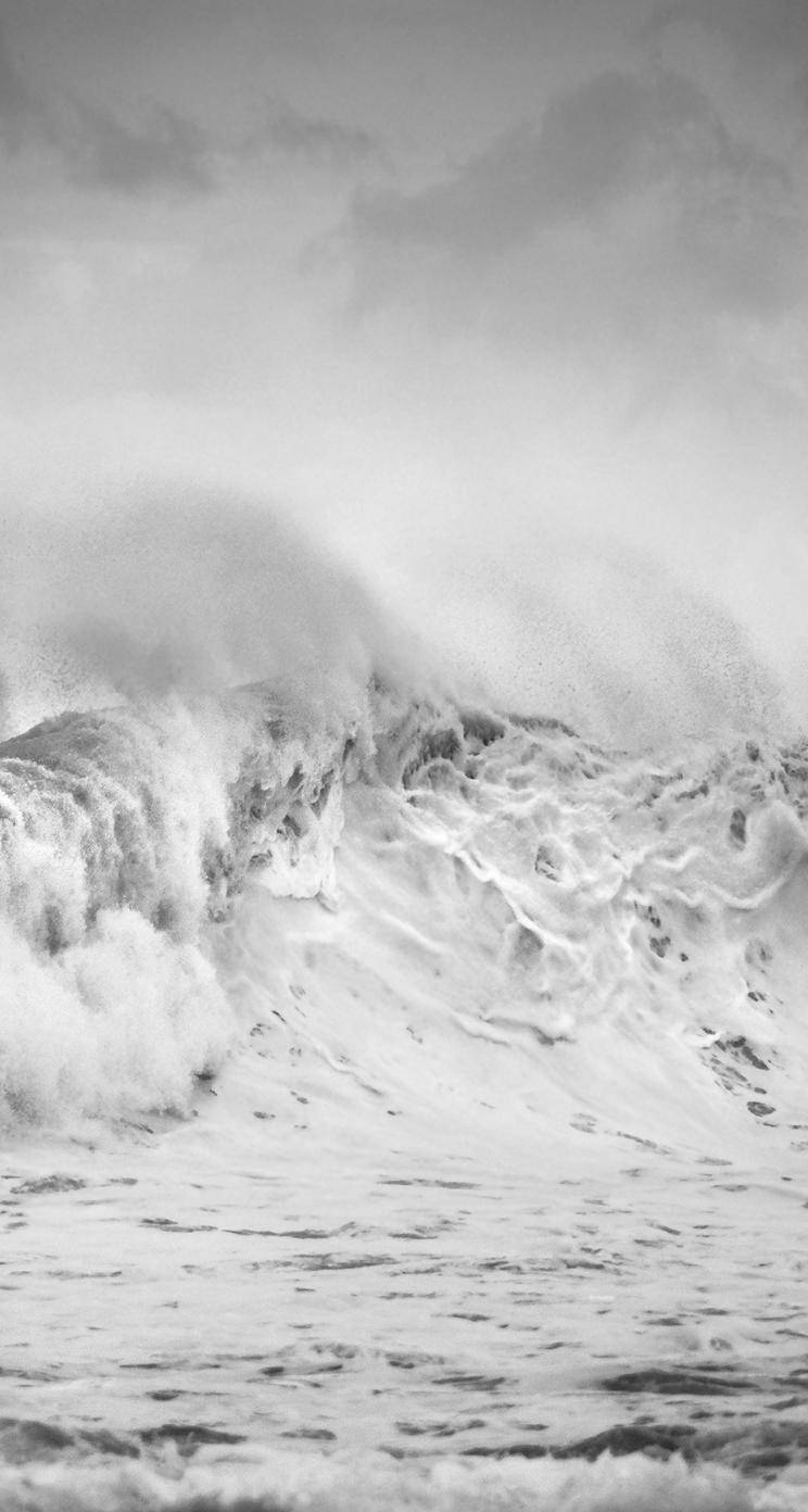 黑白iPhone海浪壁紙 壁紙 — 一張黑白照片捕捉到巨大的海浪，帶著泡沫飛沫撞向多雲的天空。