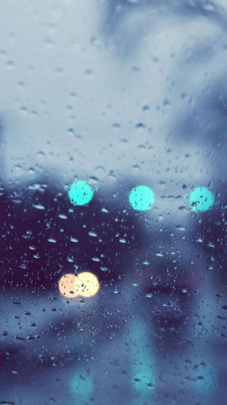 與iPhone一同欣賞雨中寧靜時光 壁紙 — 雨滴模糊了窗外的景色，遠處色彩繽紛的散景燈光柔和地閃爍。
