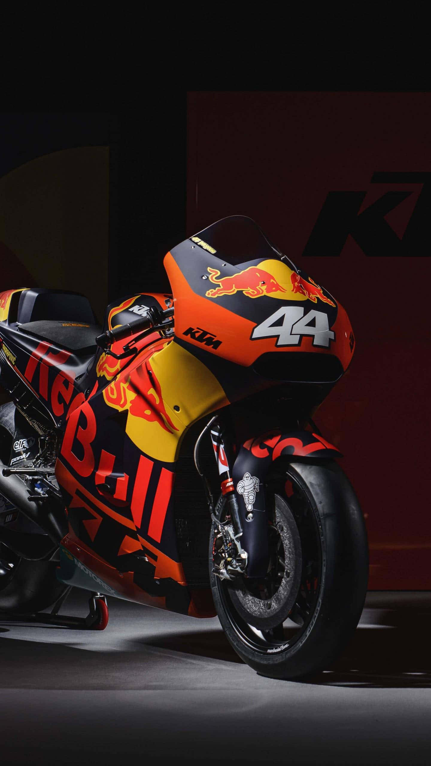 享受開闊道路，摩托車iPhone 壁紙 — 一輛帶有Red Bull塗裝和44號的時尚KTM MotoGP電單車，在戲劇性的工作室燈光下閃耀。