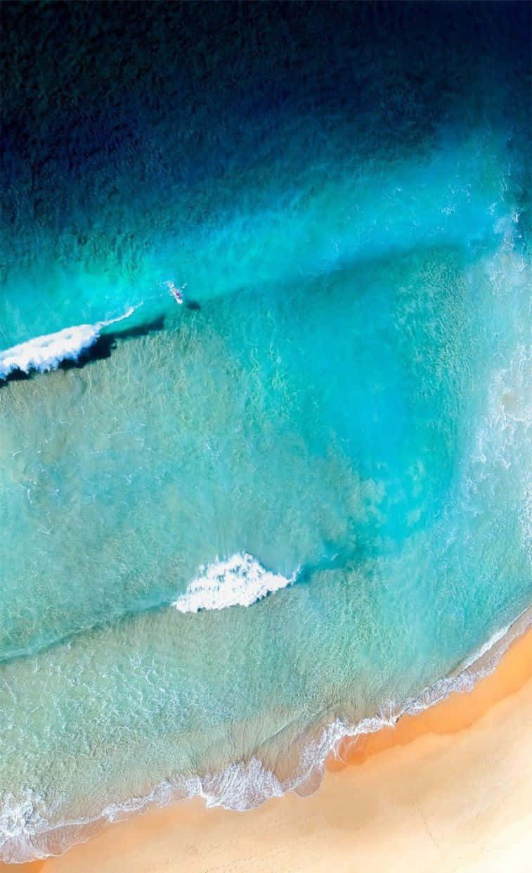 看看這款時尚青綠色iPhone！ 壁紙 — 鳥瞰圖：碧綠海浪輕輕拍打金色沙灘，一名孤獨的衝浪者正在乘風破浪。