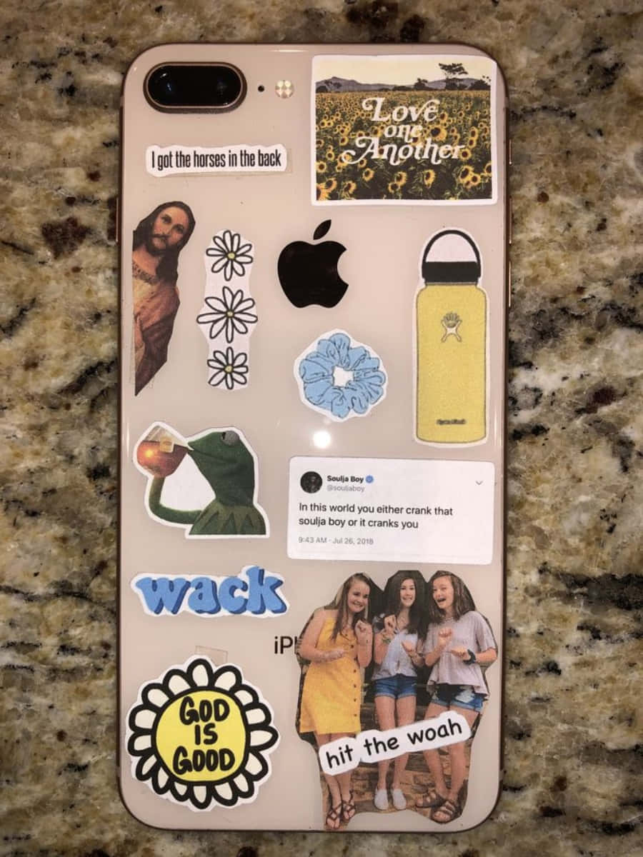 以美學 iPhone 炫耀生活，增添亮色 壁紙 — 一部手機上貼滿了彩色貼紙，包括耶穌、向日葵、青蛙和社交媒體帖子，放在花崗岩檯面上。