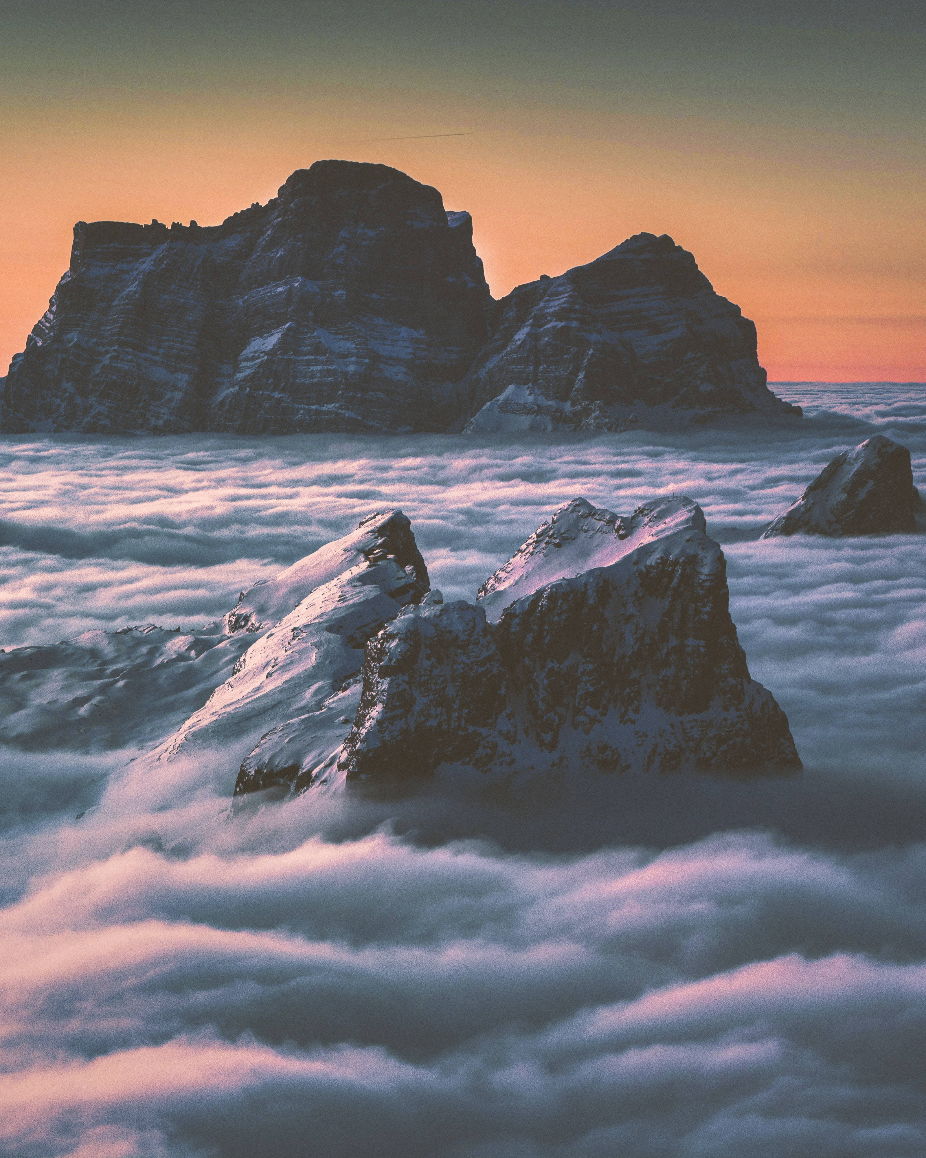 昇起山雲 iPhone 壁紙 — 白雪覆蓋的山峰在沐浴著溫暖日出色調的雲海之上巍然聳立。