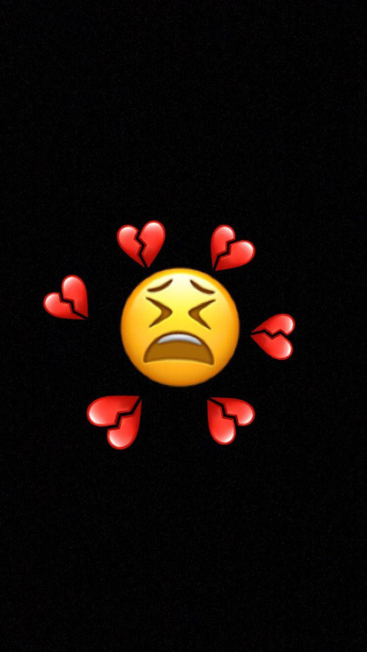 傷感表情符號與破碎心形iPhone 壁紙 — 一個黃色哭泣的表情符號，被破碎的紅色心形環繞，背景為黑色。