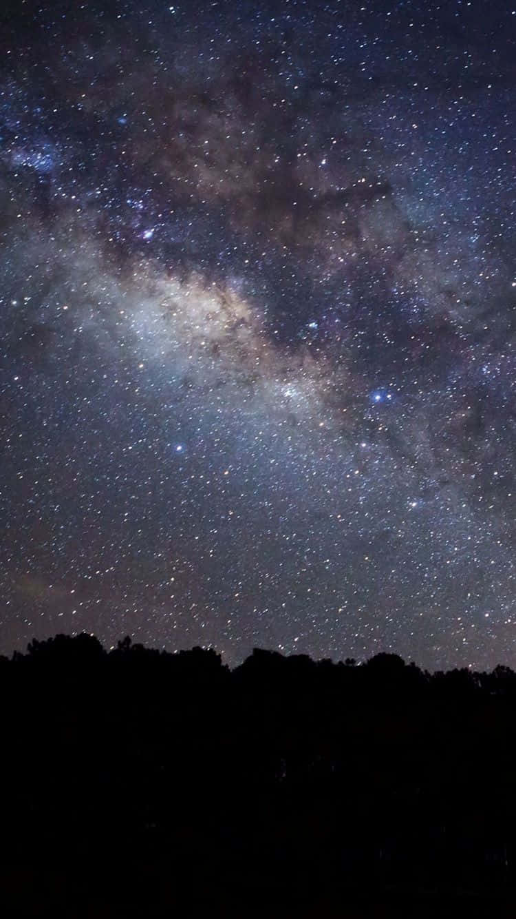 星空宇宙iPhone壁紙 壁紙 — 令人嘆為觀止的銀河系景觀，在黑暗樹木剪影上方，橫跨滿天繁星的夜空。