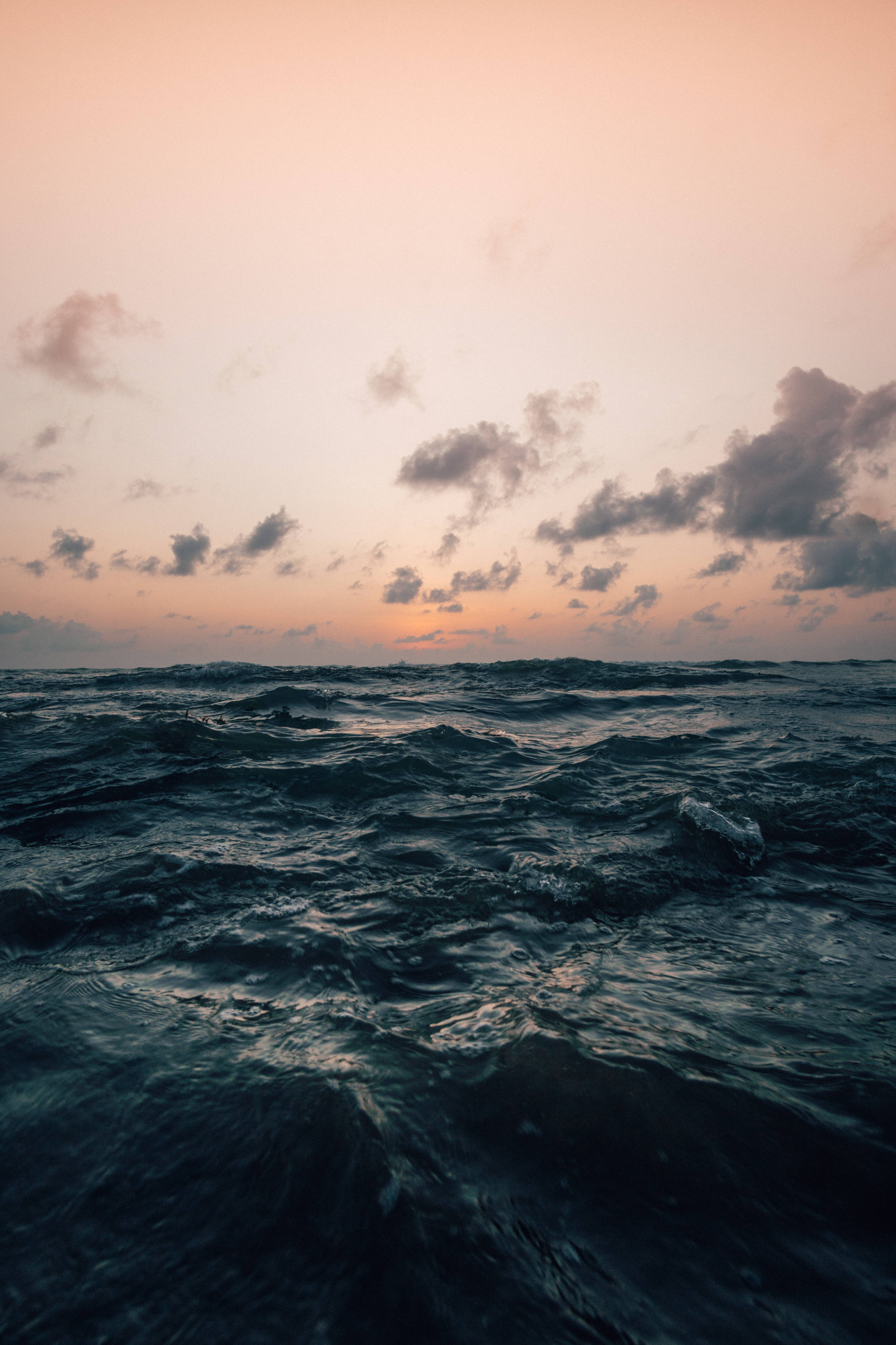 iPhone 置於復古背景 壁紙 — 廣闊的海洋，深色波浪，柔和的粉紅色和橙色日落天空，散落的雲朵。
