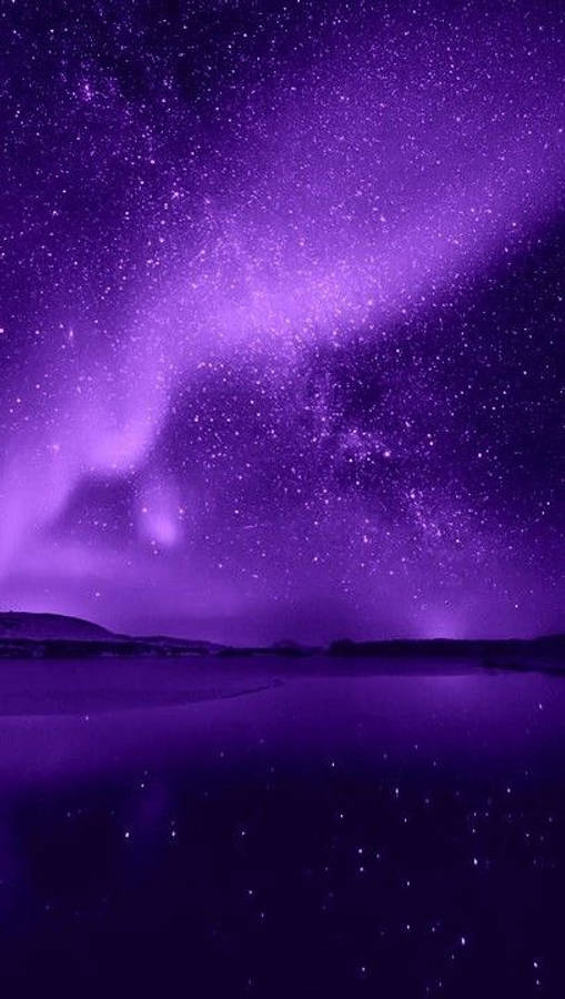 繁星與光暈的紫色星系 iPhone 壁紙 — 迷人的紫色極光在繁星點點的夜空上舞動，倒映在平靜的湖面上，遠方有山丘。