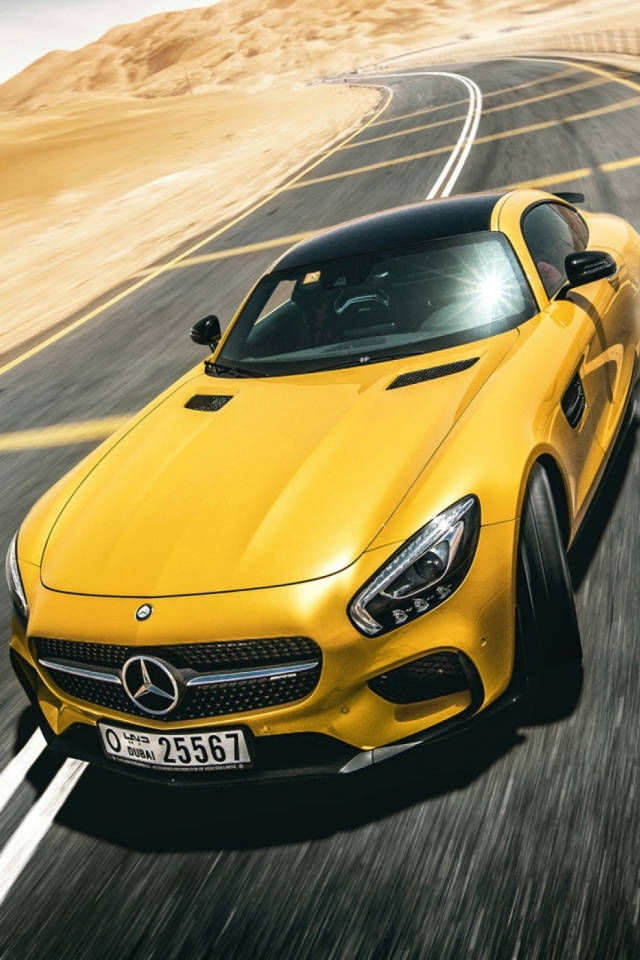 金黃色梅賽德斯 iPhone X 壁紙 — 一輛充滿活力的黃色 Mercedes-AMG GT 在明亮的日光下沿著蜿蜒的沙漠高速公路飛馳。