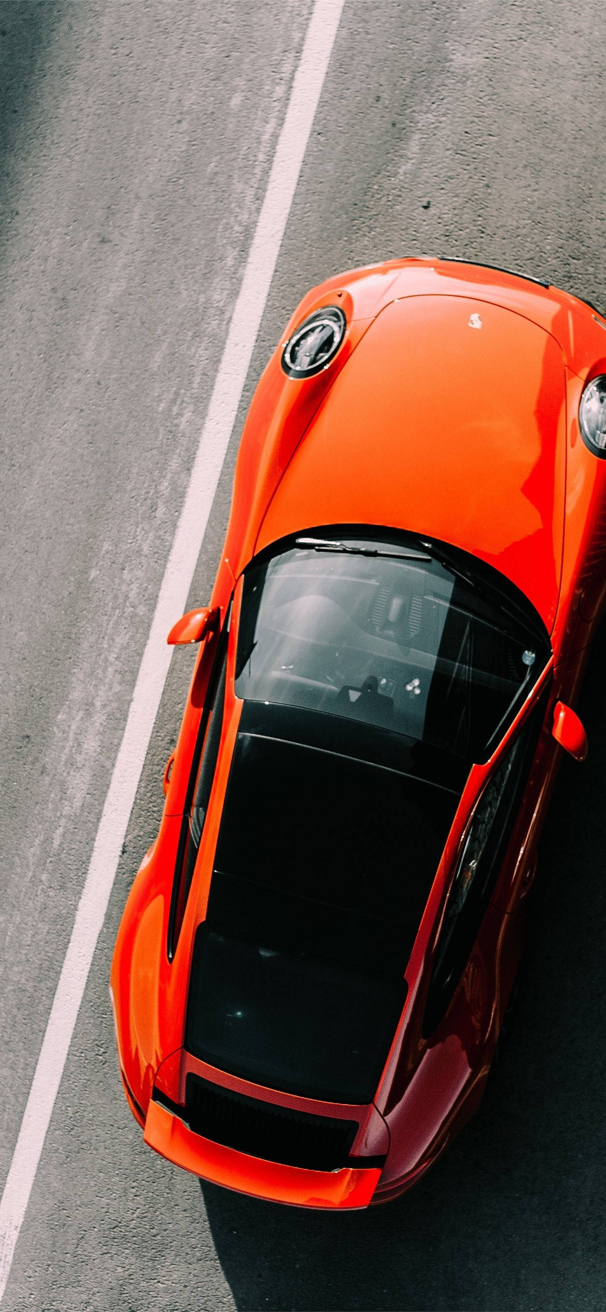 iPhone X 背景：金屬橙色保時捷 911 GT3 R 頂視角 壁紙 — 從上方俯瞰一輛鮮橙色跑車在帶有白色標線的灰色瀝青路上行駛。