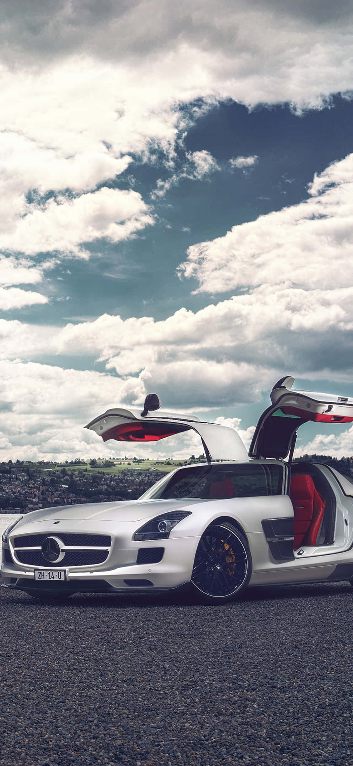 iPhone X AMG GT-R 背景 SLS AMG 開門 壁紙 — 一架白色平治 SLS AMG 跑車，鷗翼車門打開，停在碎石路上，天空烏雲密佈，氣氛戲劇化。