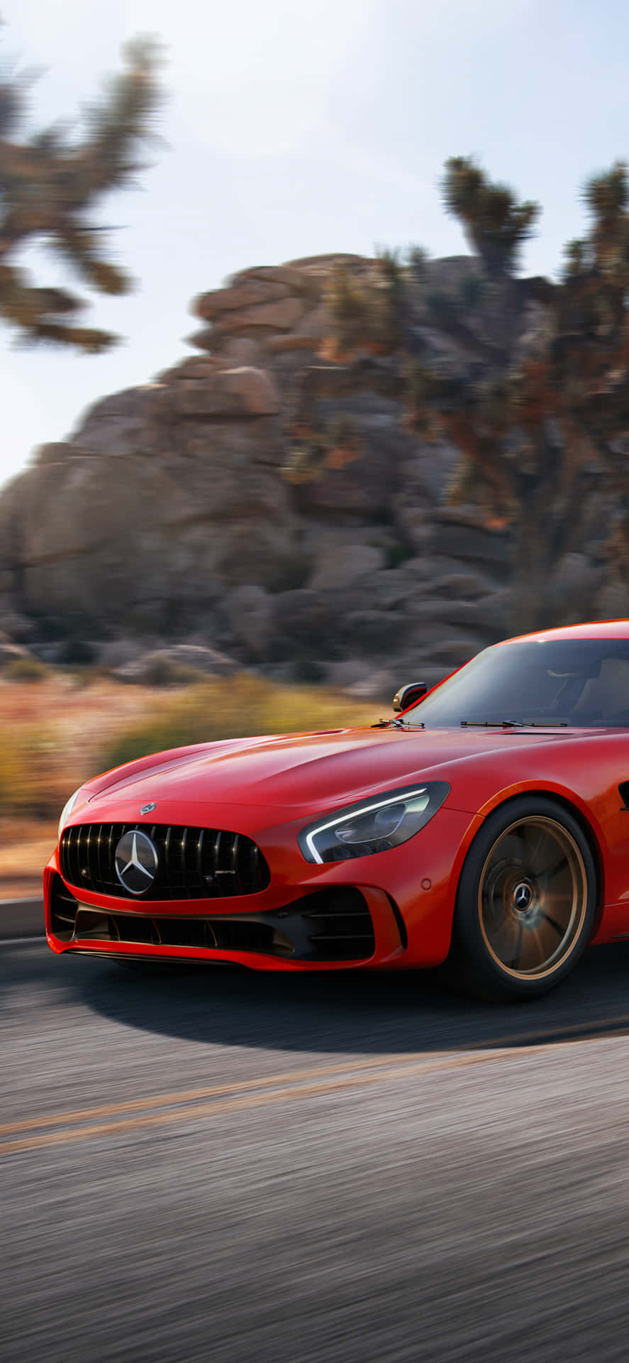 iPhone X AMG GT-R 背景 - 2018 AMG GTR 紅色前臉 壁紙 — 一輛充滿活力的紅色 Mercedes-AMG GT 在沙漠公路上疾馳，背景是模糊的岩石 formations 和約書亞樹。