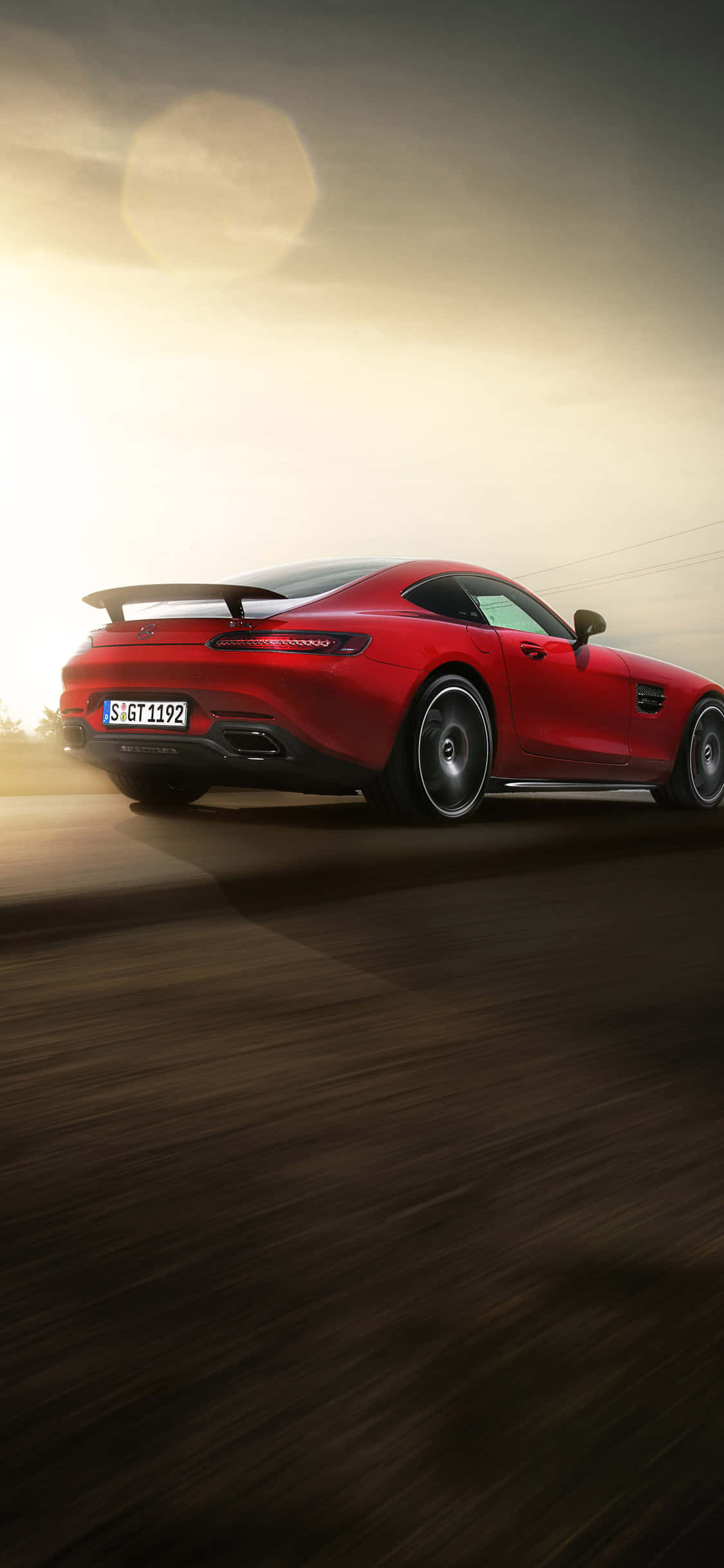 iPhone X AMG GT-R 背景紅色尾箱 AMG GT 壁紙 — 一輛鮮紅色的跑車在金色夕陽天空下，沿著模糊的道路疾馳，帶有鏡頭光暈。
