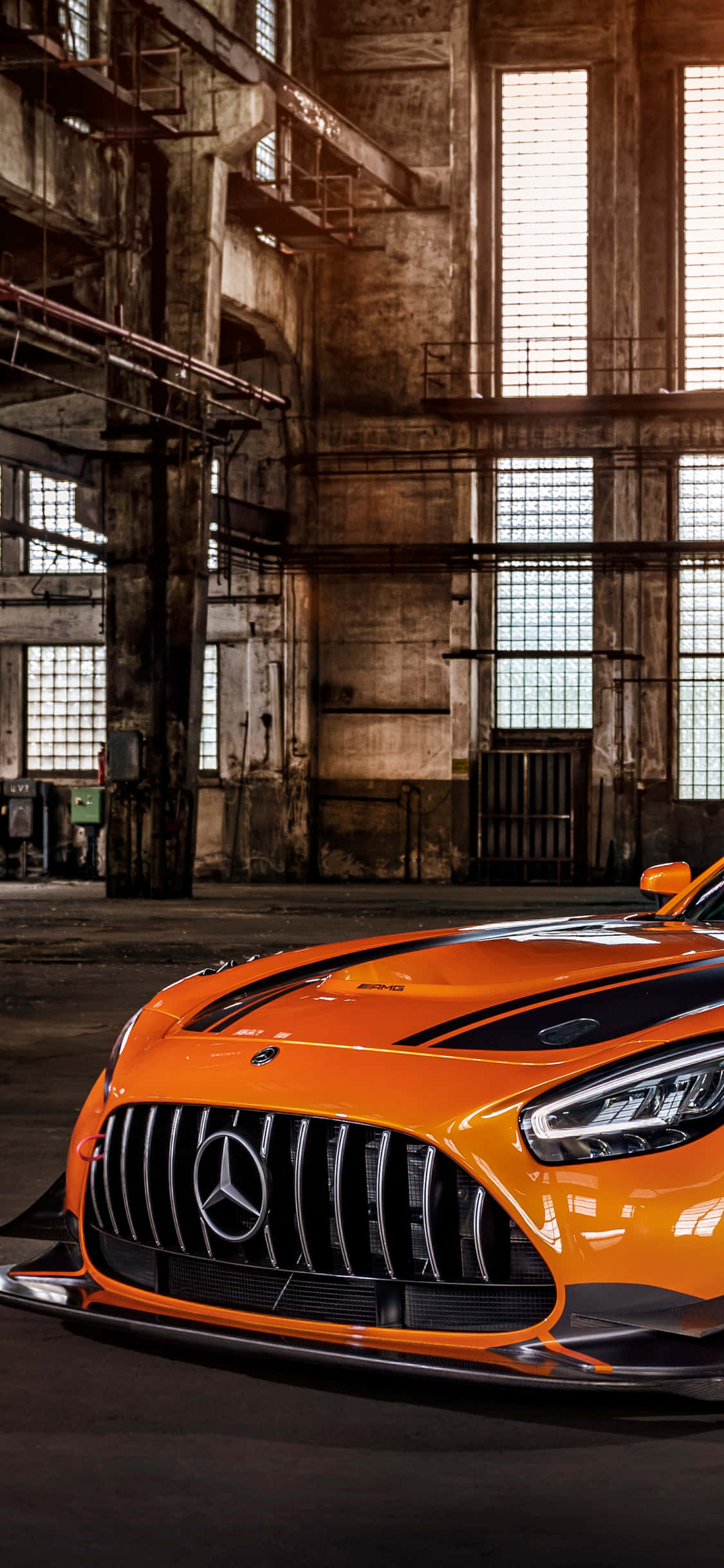 iPhone X AMG GT-R 背景：橙色 AMG GT 停泊於廢棄倉庫 壁紙 — 一輛充滿活力的橙色 Mercedes-AMG GT R 跑車在破舊倉庫的工業天窗下閃閃發光。