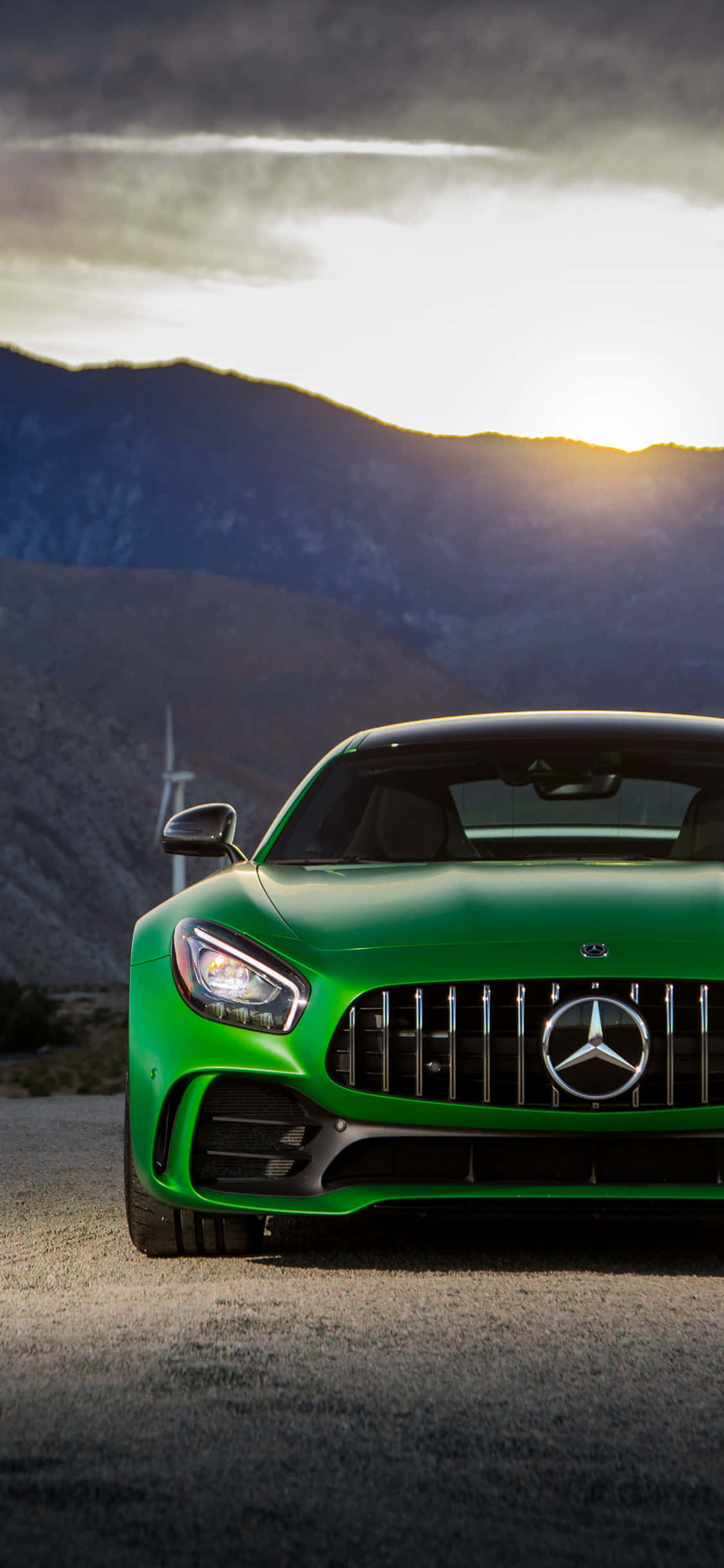 iPhone X AMG GT-R 背景 綠色 AMG GT 車頭 壁紙 — 一架充滿活力的綠色Mercedes-AMG GT跑車停泊在山路上，夕陽西下，雲彩壯麗。