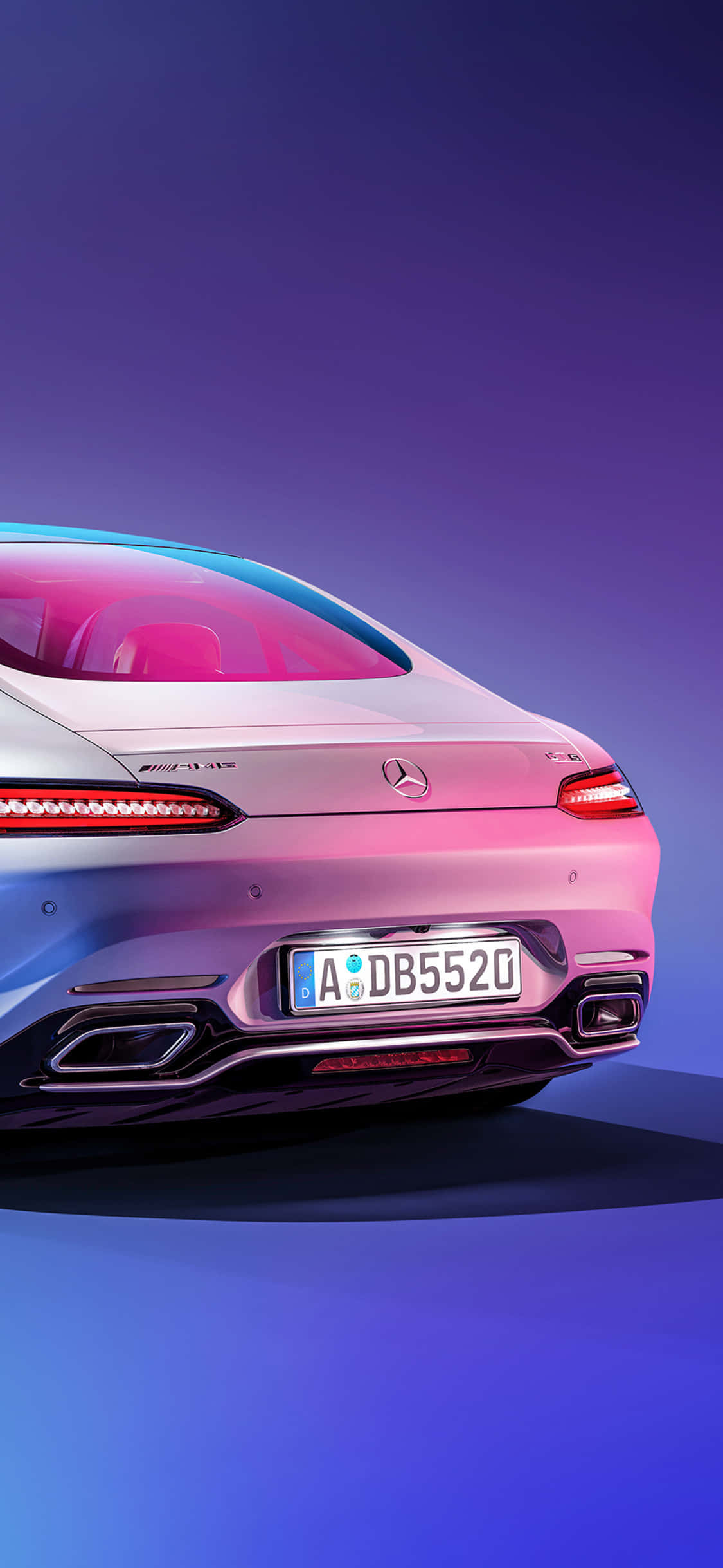 iPhone X AMG GT-R 背景白色尾箱 AMG GT 壁紙 — 一輛時尚的銀色Mercedes-AMG S 63轎車在充滿活力的紫色和藍色工作室燈光下閃耀，展示其後部設計和運動型排氣管。