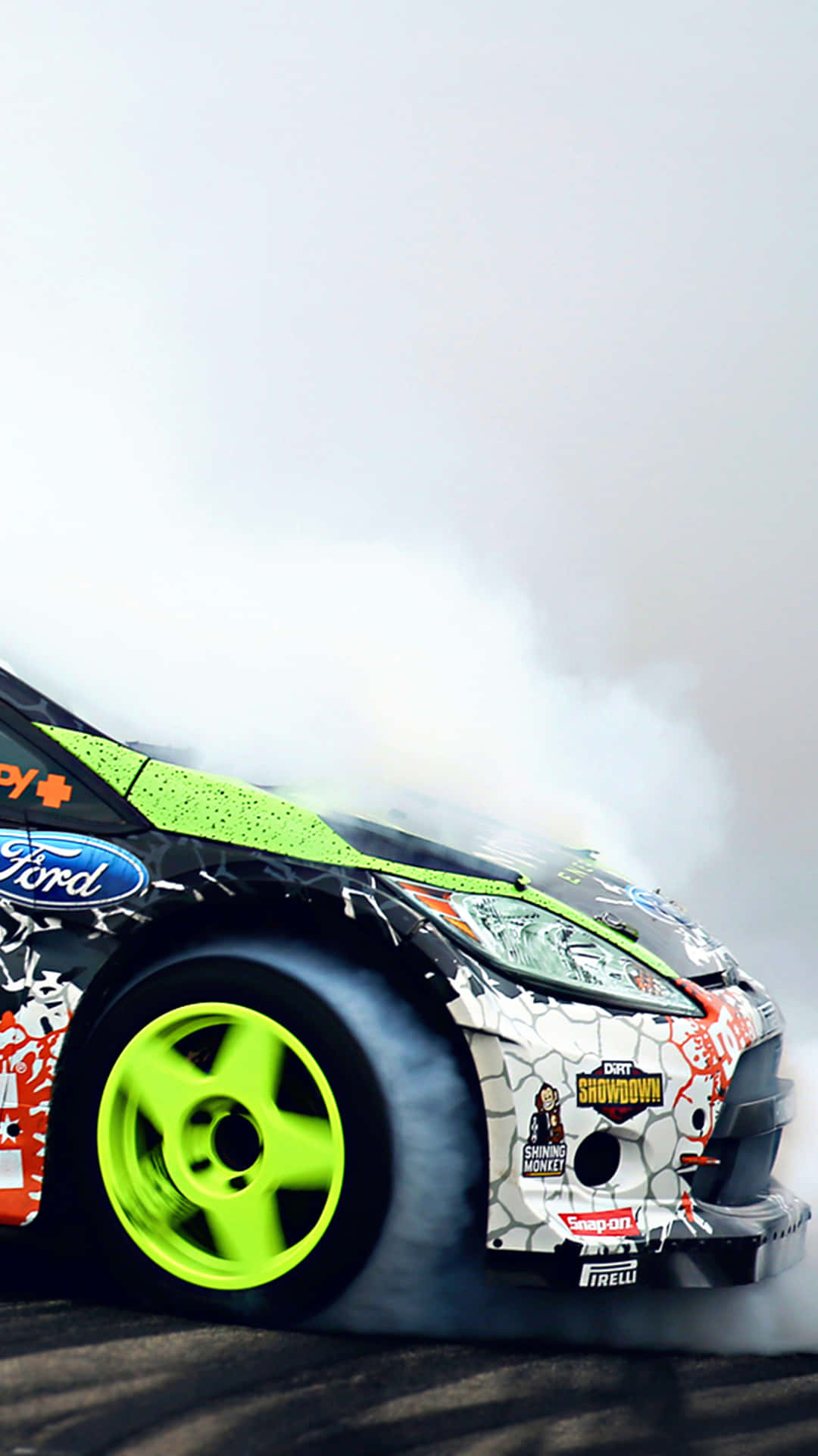 iPhone X《Dirt Showdown》福特Fiesta RS WRC背景 壁紙 — 一輛福特飄移車，配有螢光綠色車輪和塗鴉風格貼紙，在賽道上橫滑時冒出大量濃煙。