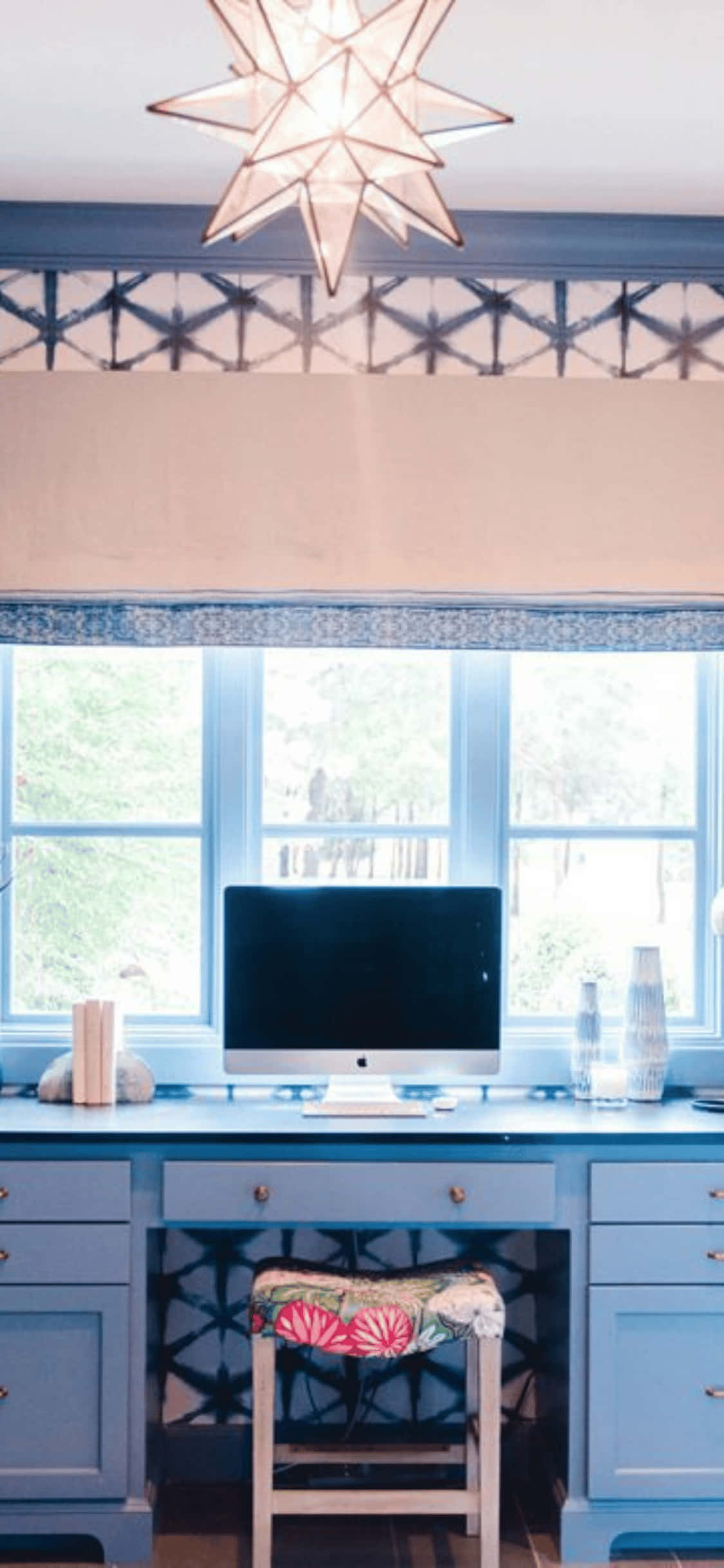 iPhone X 辦公室背景：藍色桌上的iMac 壁紙 — 寧靜的藍色家庭辦公室，配有星爆吊燈、圖案牆紙和窗下的花卉凳子。