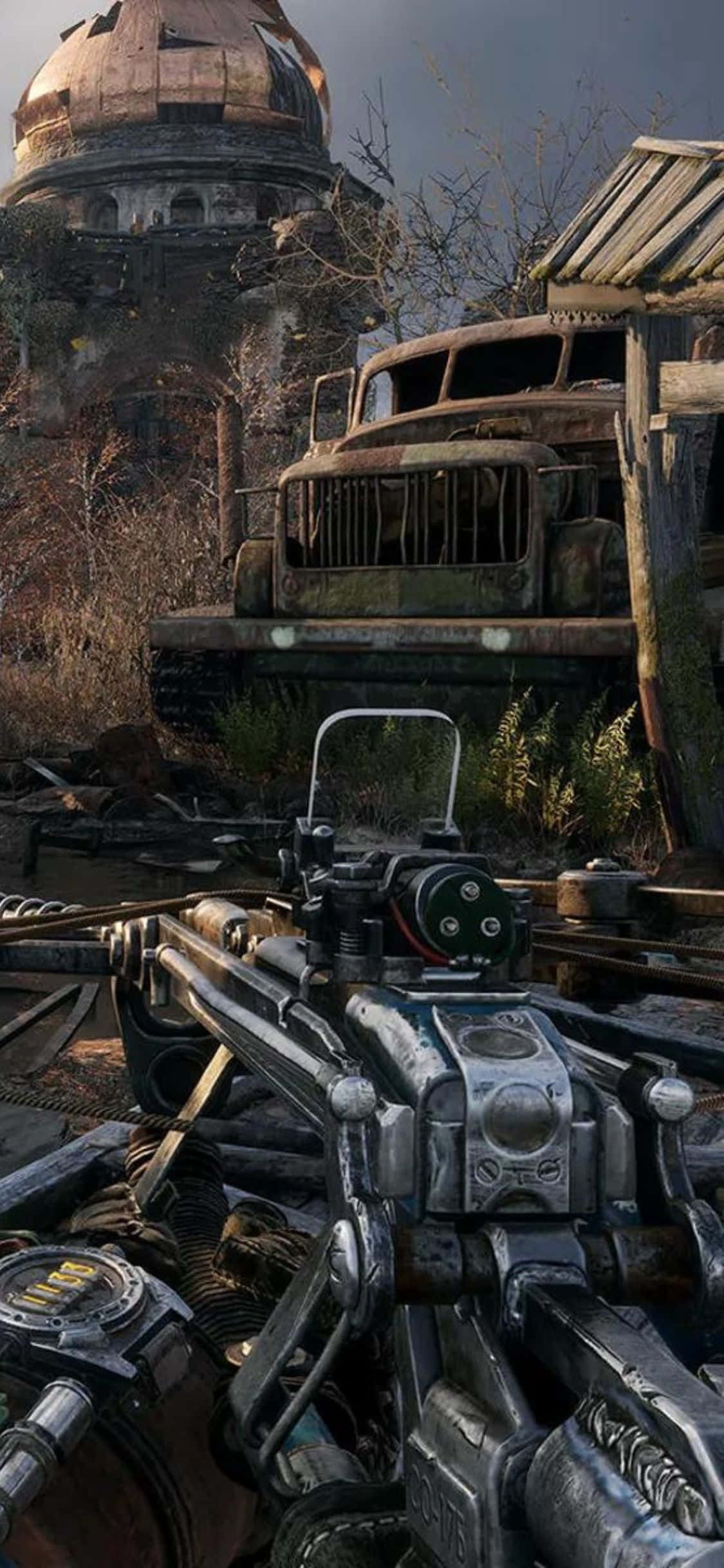 以 iPhone X 探索《Metro Exodus》的俄羅斯之外 壁紙 — 後末日荒原中，一把未來武器瞄準一輛生鏽卡車旁邊正在崩塌的圓頂建築的第一人稱視角。