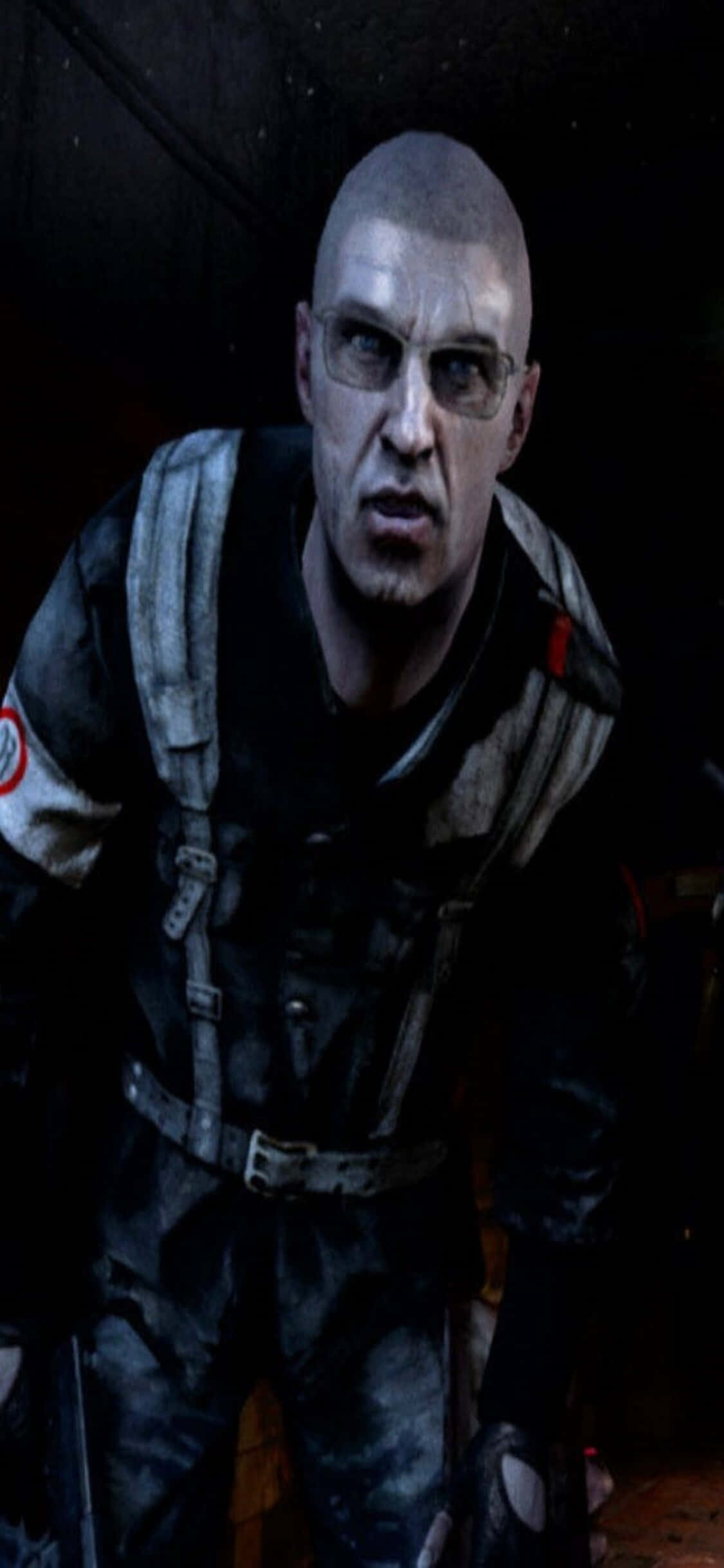 在 iPhone X 上體驗《Metro Last Light》的驚心動魄戰鬥 壁紙 — 一個光頭男子身穿戰術裝備，戴著眼鏡，在昏暗的環境中凝視著。