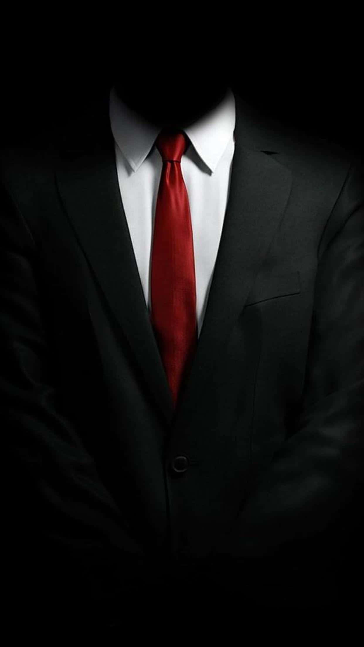 iPhone X 上的《Hitman 2》精準潛行動作 壁紙 — 一個神秘人物身穿黑色西裝和紅色領帶，站在黑暗中，臉部被陰影遮蓋。