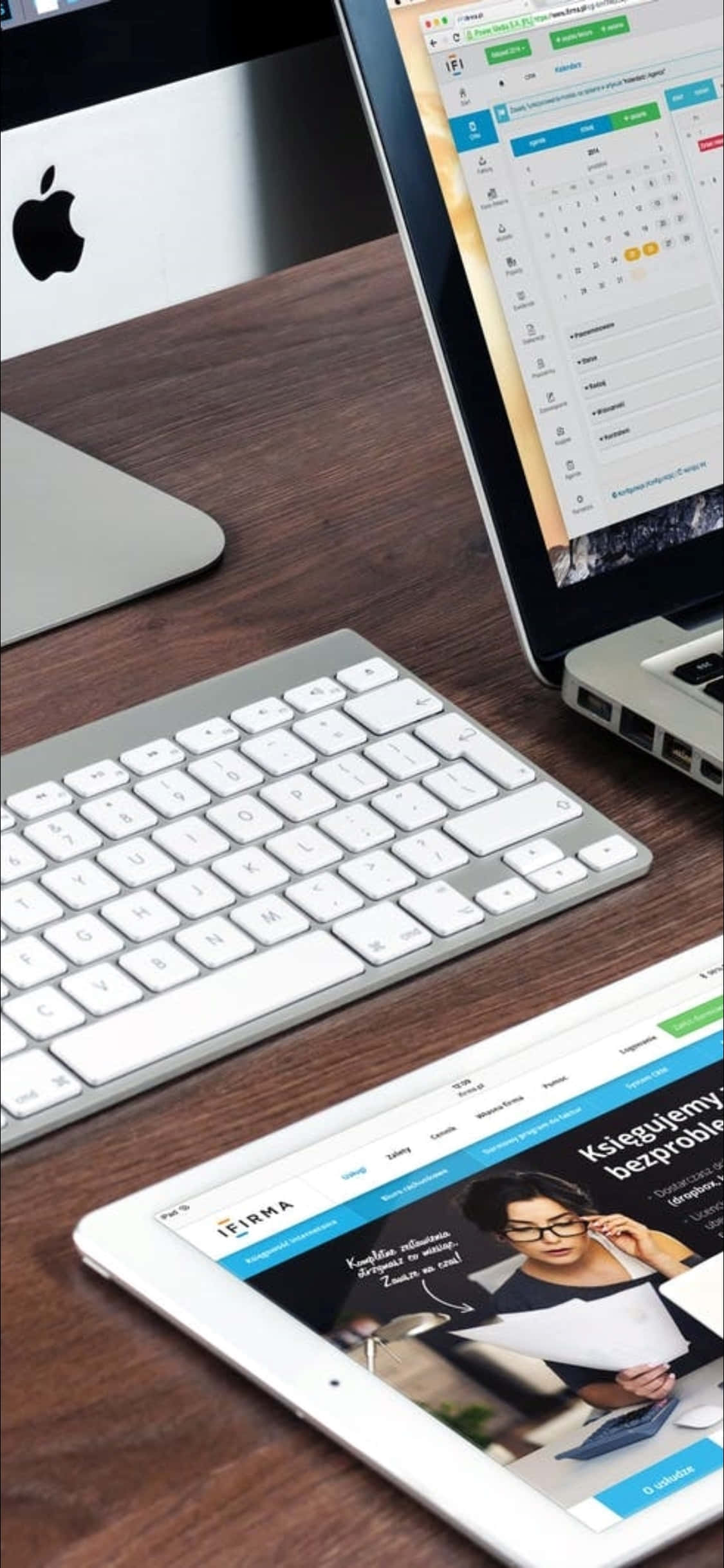 iPhone X 桌面背景：筆記本電腦與鍵盤 壁紙 — 現代工作空間，深色木桌上擺放銀色手提電腦、平板電腦和鍵盤，顯示數碼內容。