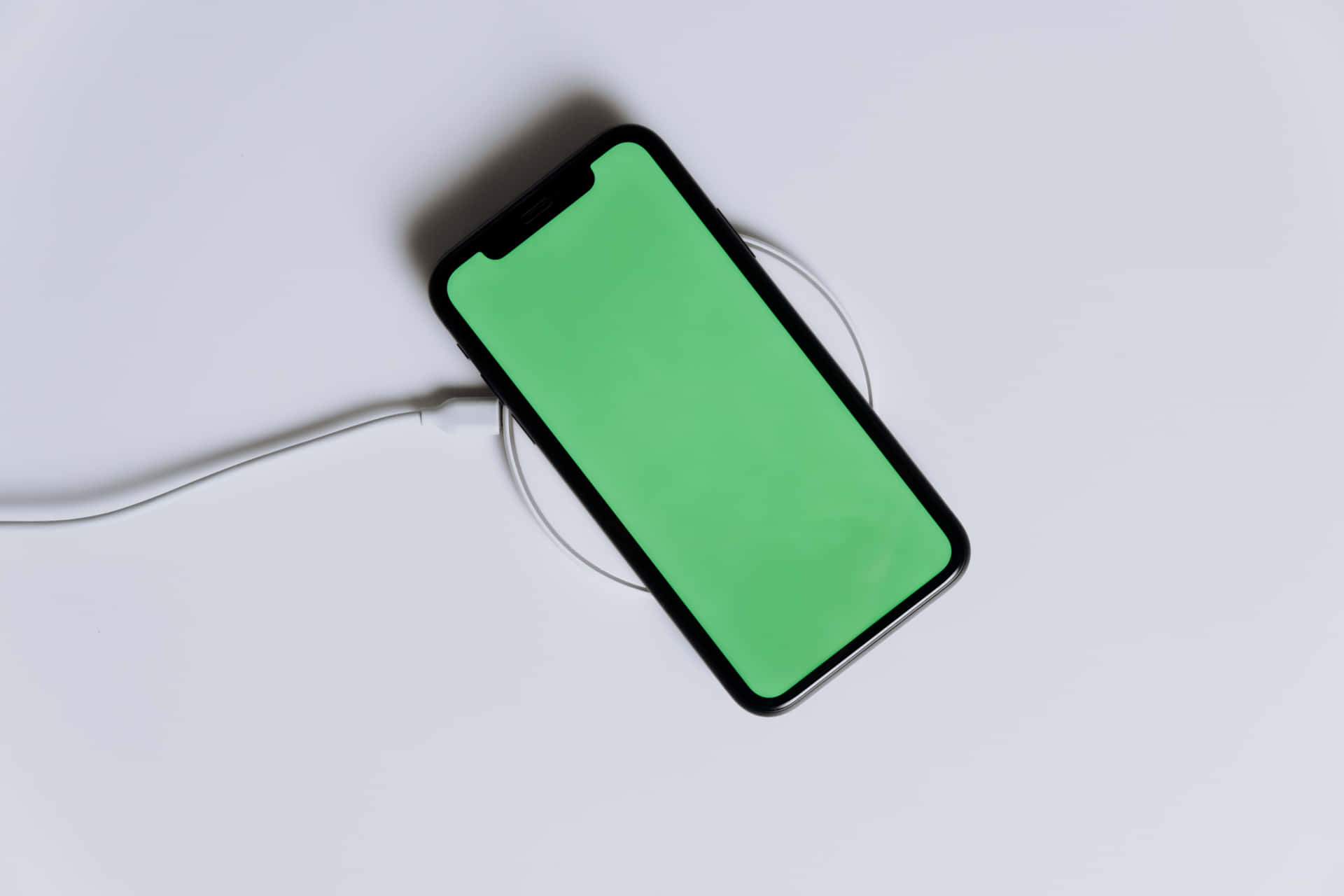 黑色智能手機在白色充電板上充電，帶綠色屏幕