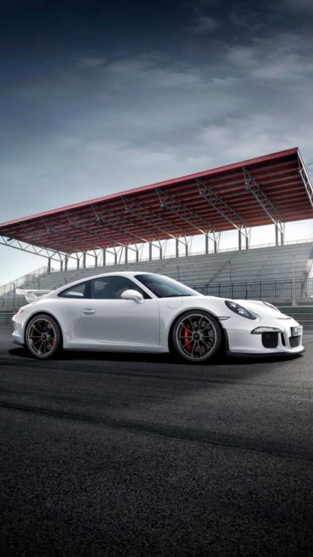 白色保時捷911 GT3 RS在賽道上，背景有紅色頂篷看台和多雲天空