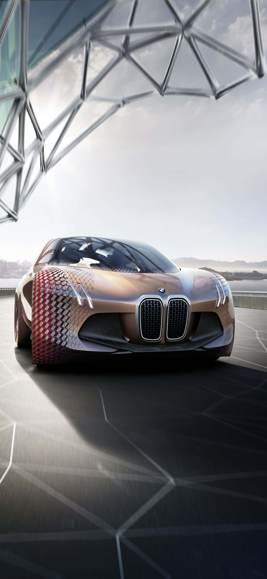 iPhone X 與背景中的 BMW，是奢華生活的完美象徵 壁紙 — 一輛未來感十足的BMW概念車，帶有幾何紅色和古銅色圖案，停放在金屬網格結構下的時尚平台上。