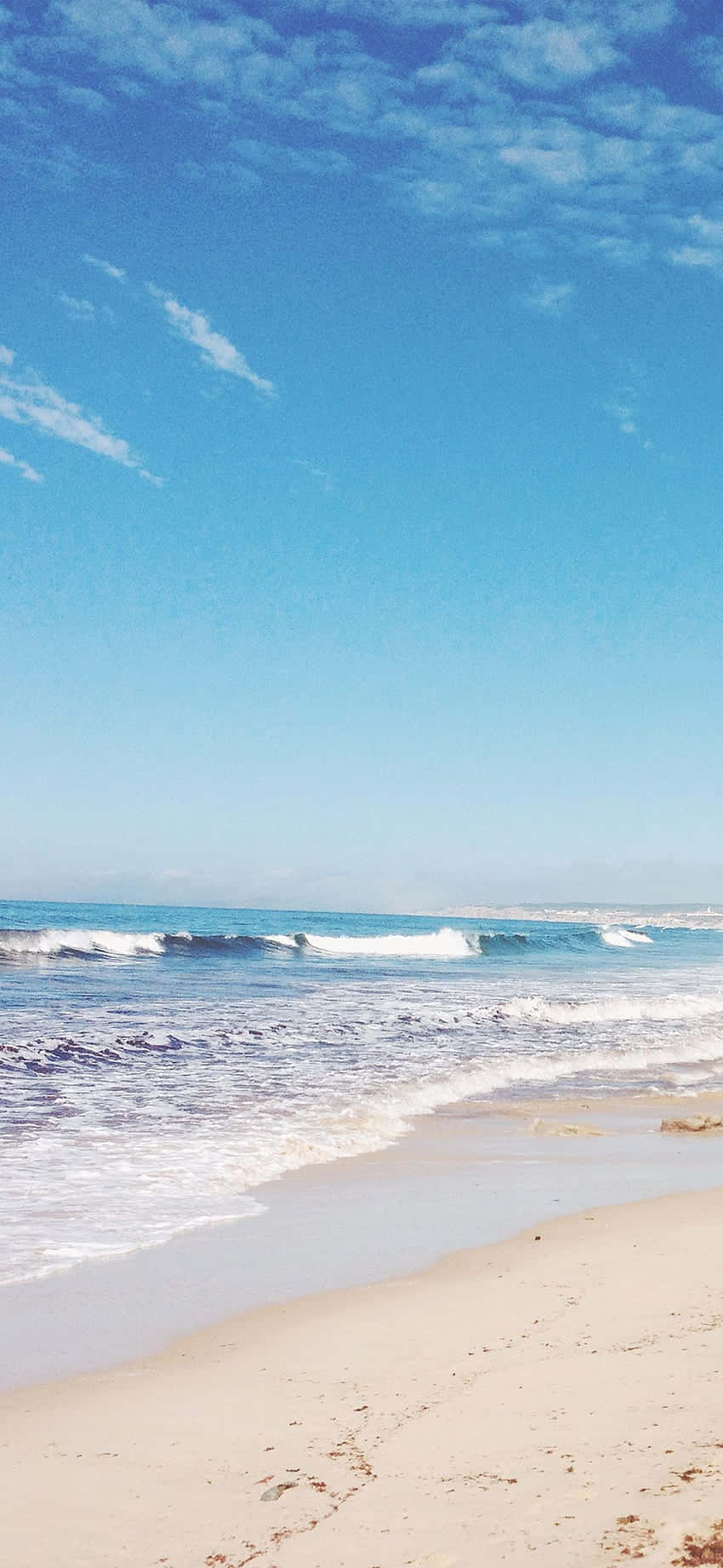 iPhone X 馬利布背景 白色沙灘 壁紙 — 寧靜的海灘場景，碧綠色的海浪拍打著金色沙灘，廣闊的藍天中飄著縷縷白雲。