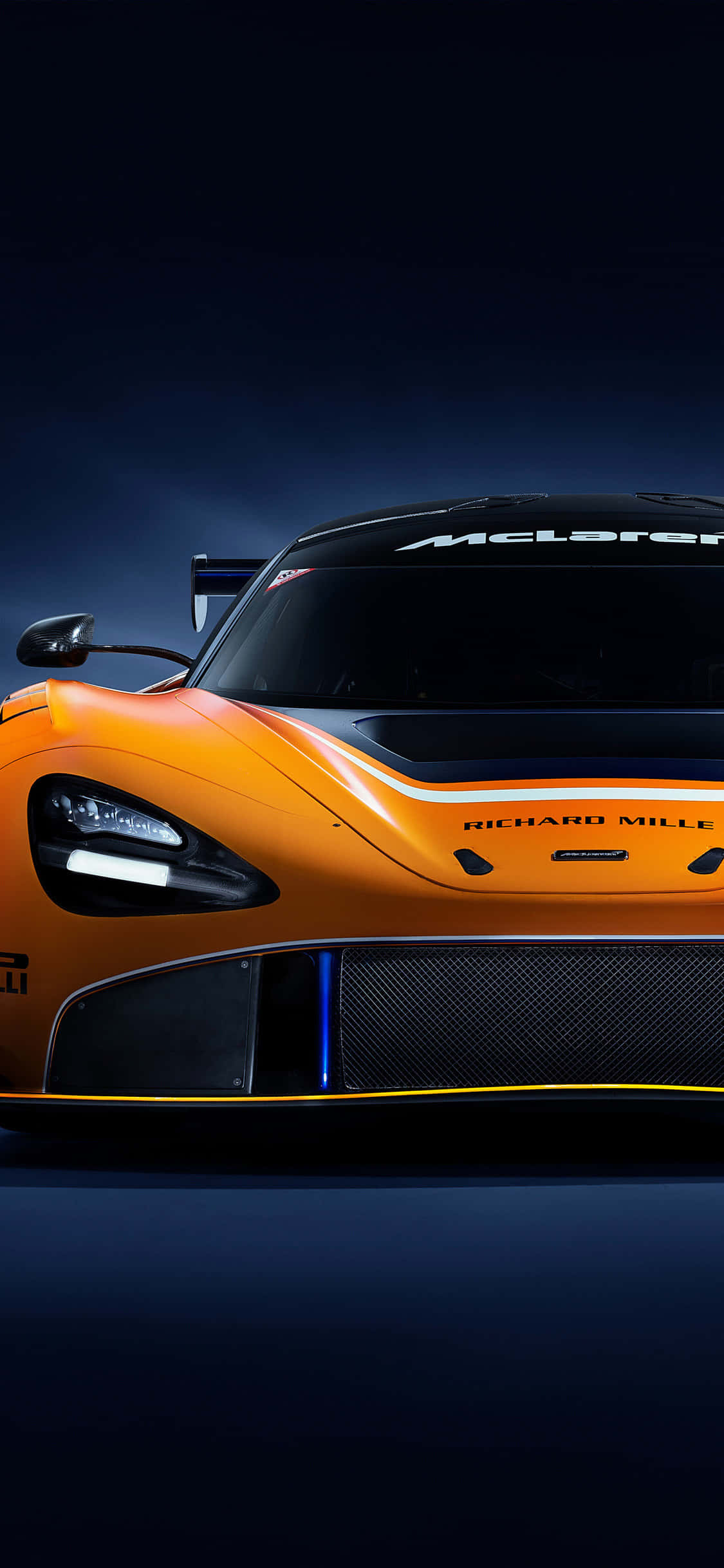 iPhone X 麥拉倫 720S GT3 賽車背景 壁紙 — 一輛時尚的橙色McLaren賽車，帶有黑色飾邊和發光的藍色燈光，在黑暗背景下以戲劇性的低角度拍攝。