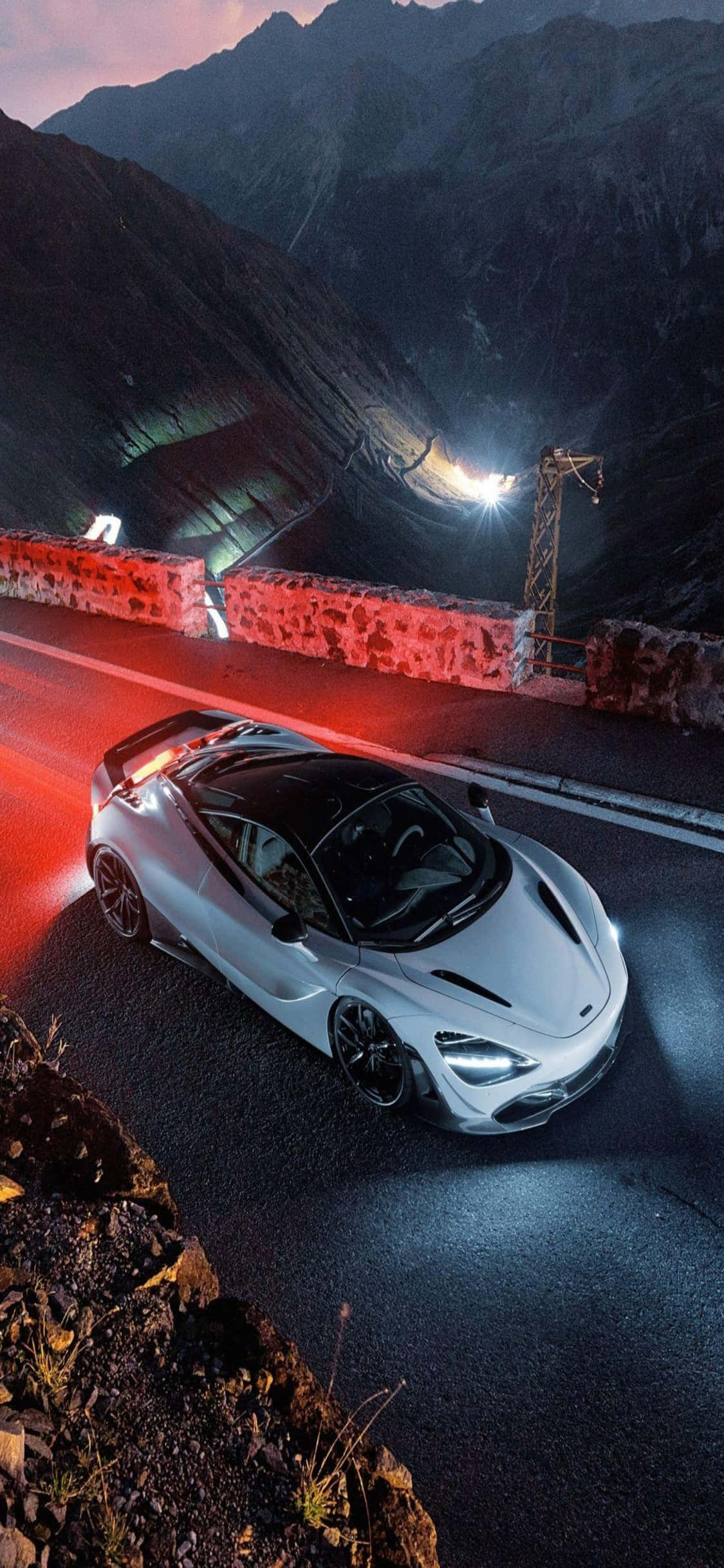 iPhone X 麥拉倫 720S 白色跑車夜景背景 壁紙 — 一輛銀色跑車在黃昏時分沿著蜿蜒的山路行駛，帶有發光的紅色尾燈和戲劇性的燈光。