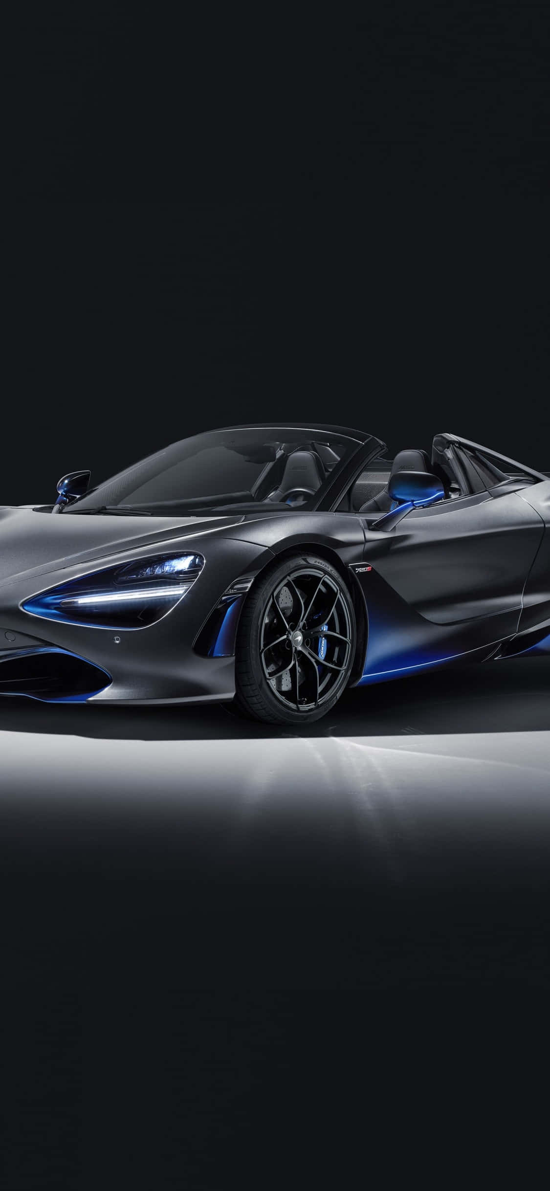 iPhone X 麥拉倫 720S 黑色模型車背景 壁紙 — 一輛時尚的啞光灰色McLaren 720S Spider，帶有發光的藍色點綴，停放在黑色背景的反射表面上。