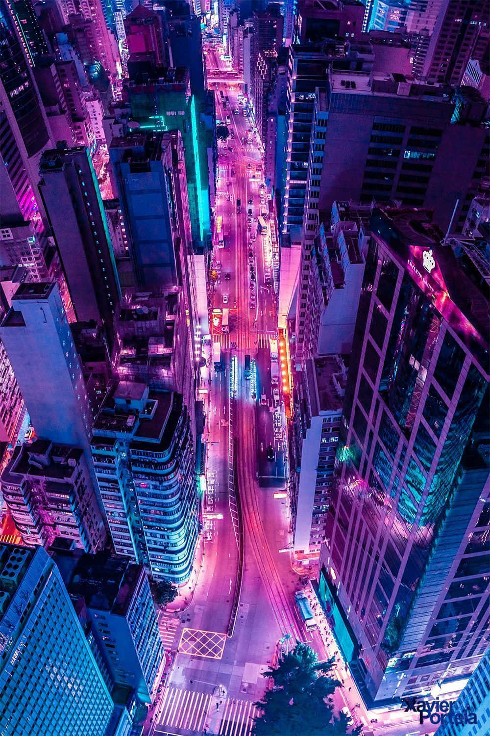 為你的 iPhone 搭配生動霓虹背景 壁紙 — 夜晚被霓虹燈淹沒的城市街道鳥瞰圖，高聳的摩天大樓散發著電光紫和藍色調。