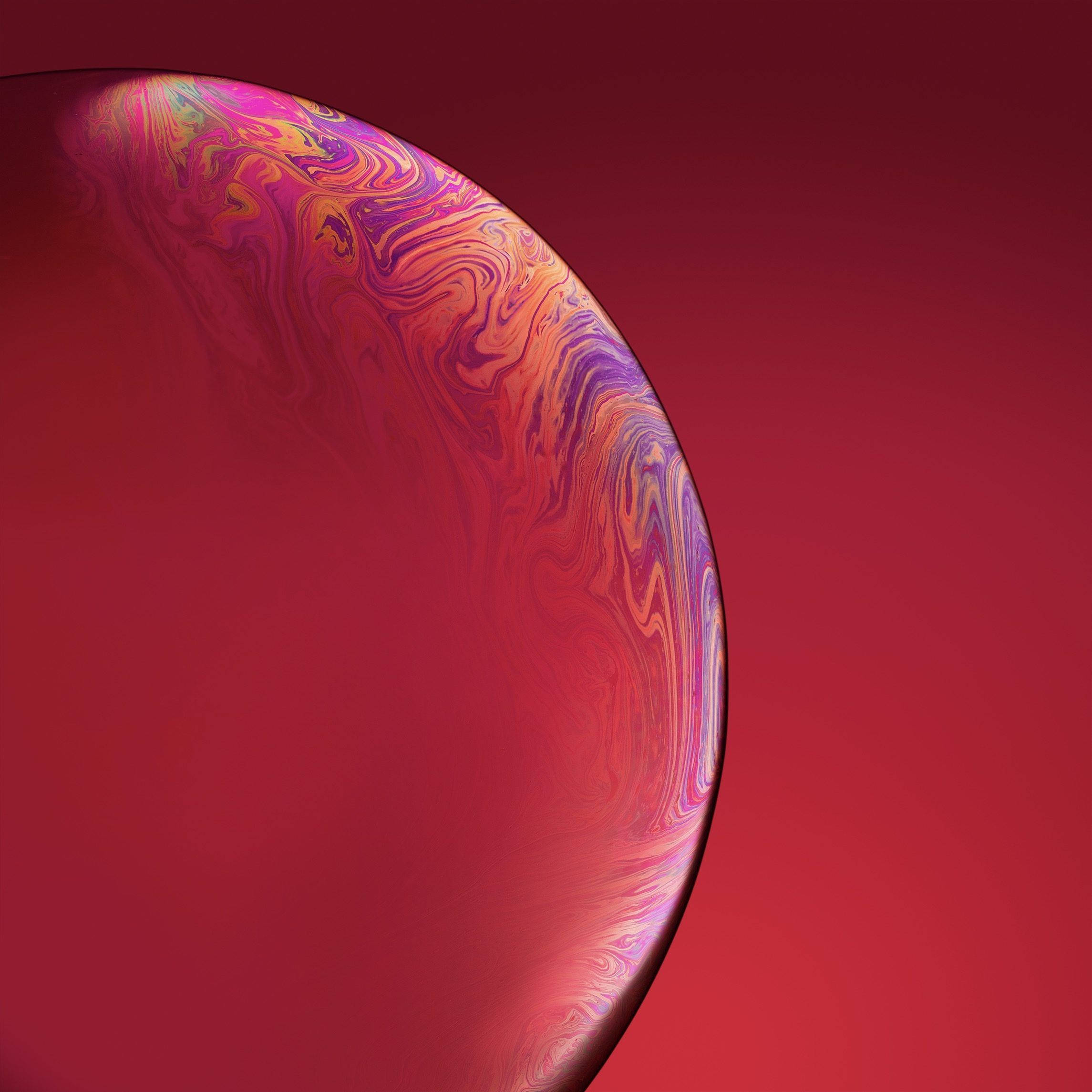 大膽紅色 iPhone XR 壁紙 — 一個充滿活力的旋轉肥皂泡，帶有虹彩粉紅色、紫色和橙色色調，漂浮在深紅色漸變背景上。