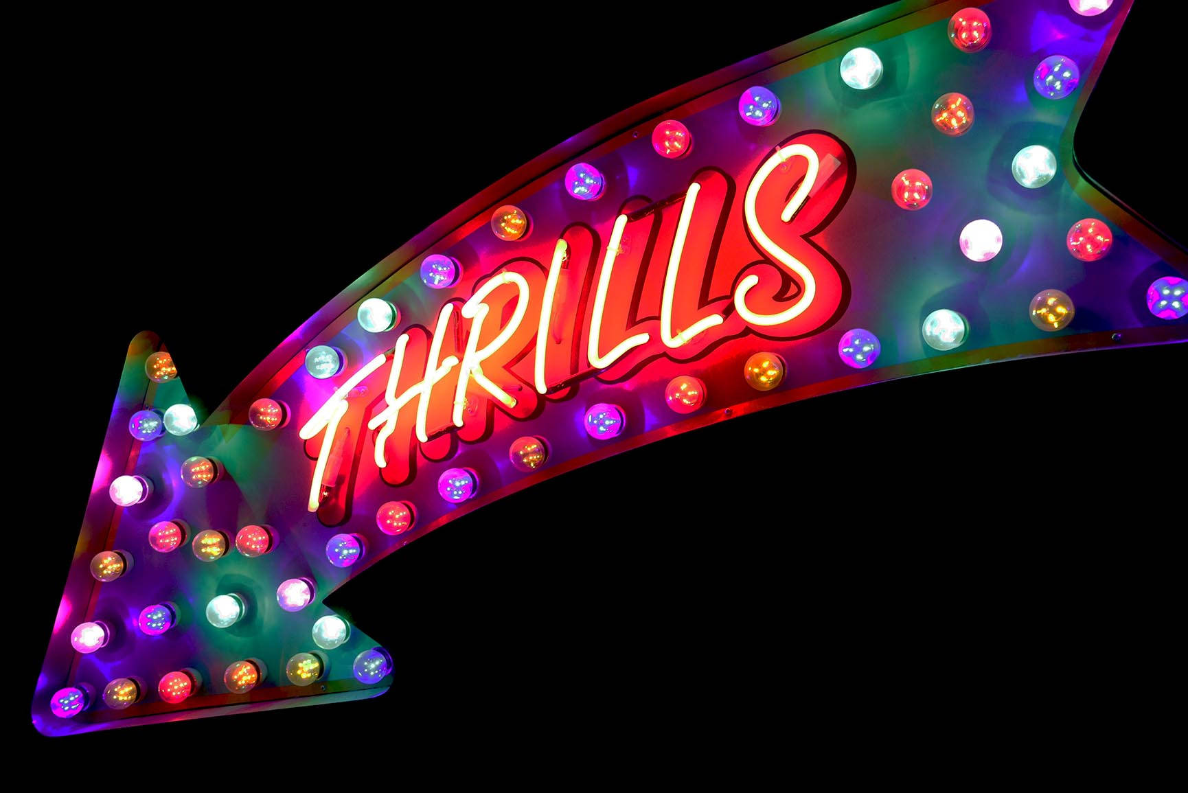 一個發光的霓虹箭頭標誌，上面有亮紅色字母 'THRILLS'。
