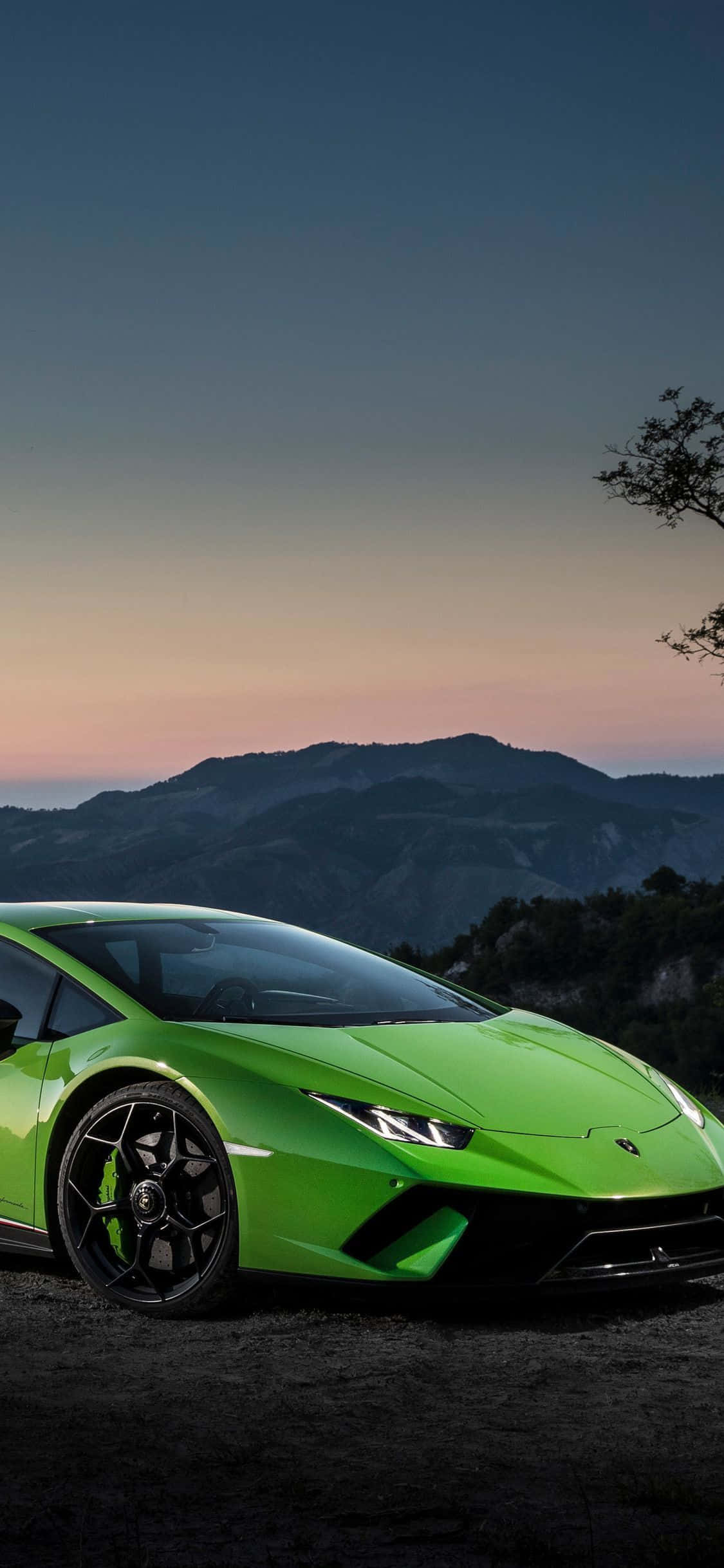 iPhone XS《狂野飆車：復仇》賽車背景 - 淺綠色 2018 蘭博基尼 Huracan 壁紙 — 一架鮮綠色林寶堅尼Huracán停泊在暮色中的山路上，背景有剪影般的山丘和柔和粉紅色的天空。