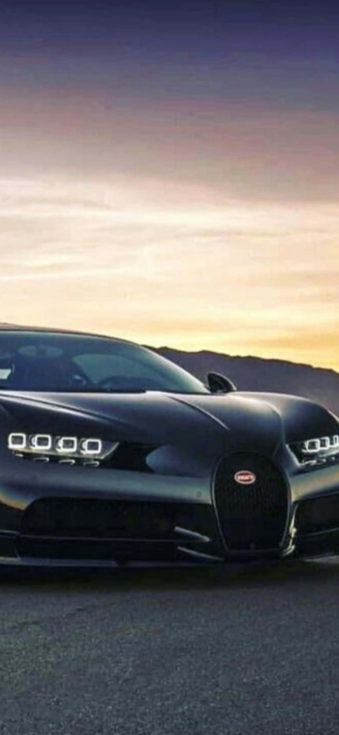 iPhone XS Bugatti：奢華與科技的巔峰結合 壁紙 — 一輛時尚的黑色Bugatti Chiron停在瀝青路上，背景是 vibrant 的日落天空和遠山。