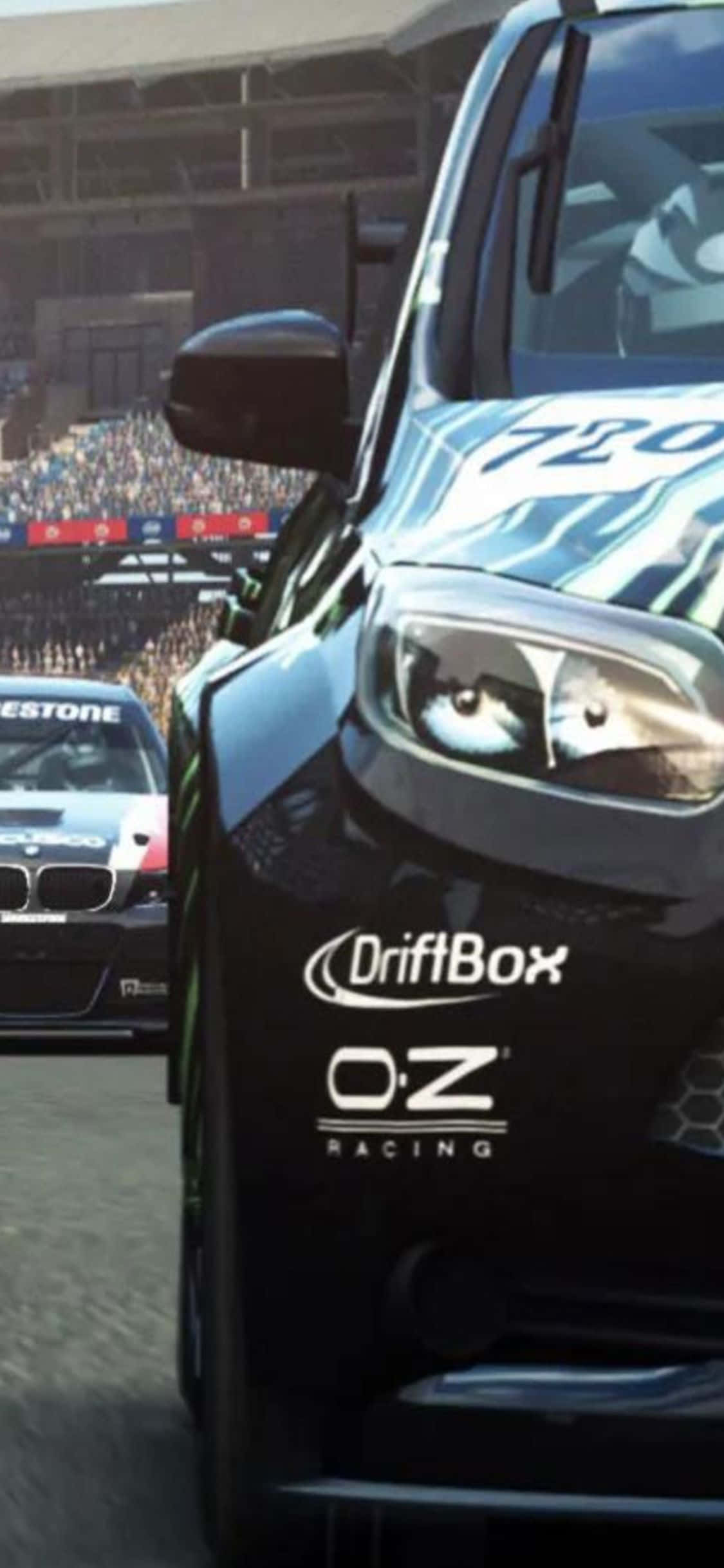 iPhone XS《Grid Autosport》飄移賽車遊戲背景 壁紙 — 一輛帶有 'DriftBox' 和 'O:Z Racing' 貼紙的黑色漂移車在賽道上比賽，背景有群眾。